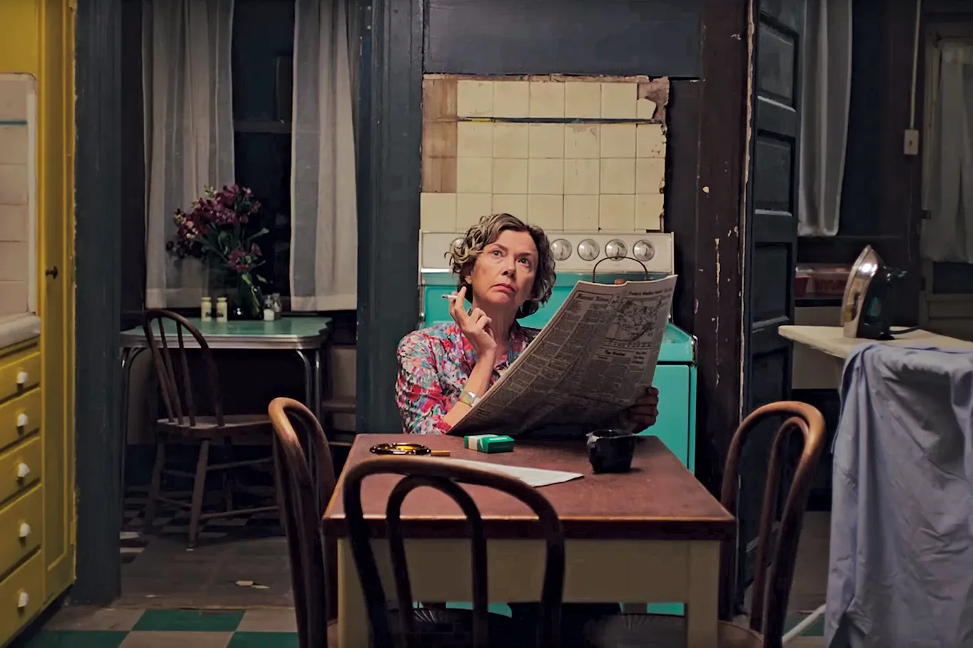 Film still: woman at kitchen table reading newspaper