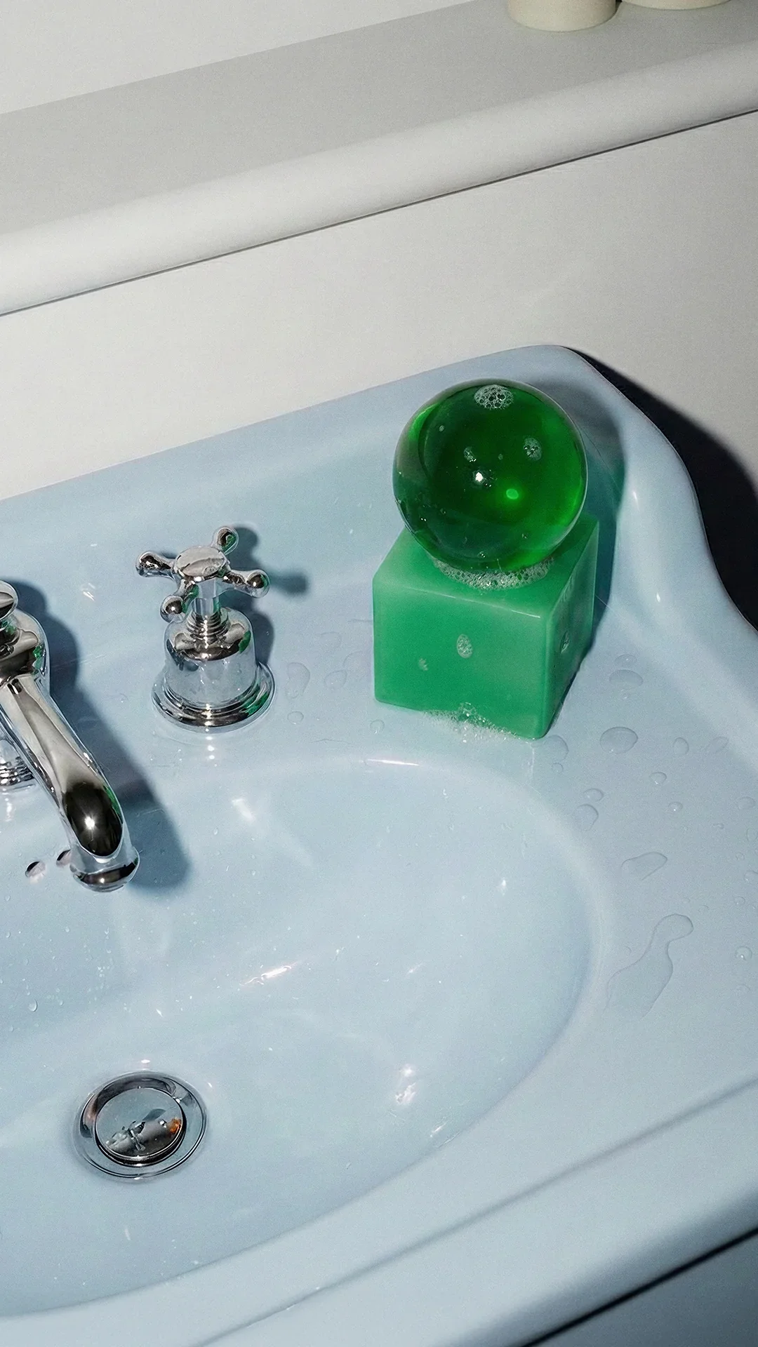 A bathroom sink with a green decorative ball on a green block, shiny silver faucet, and drainage hole.