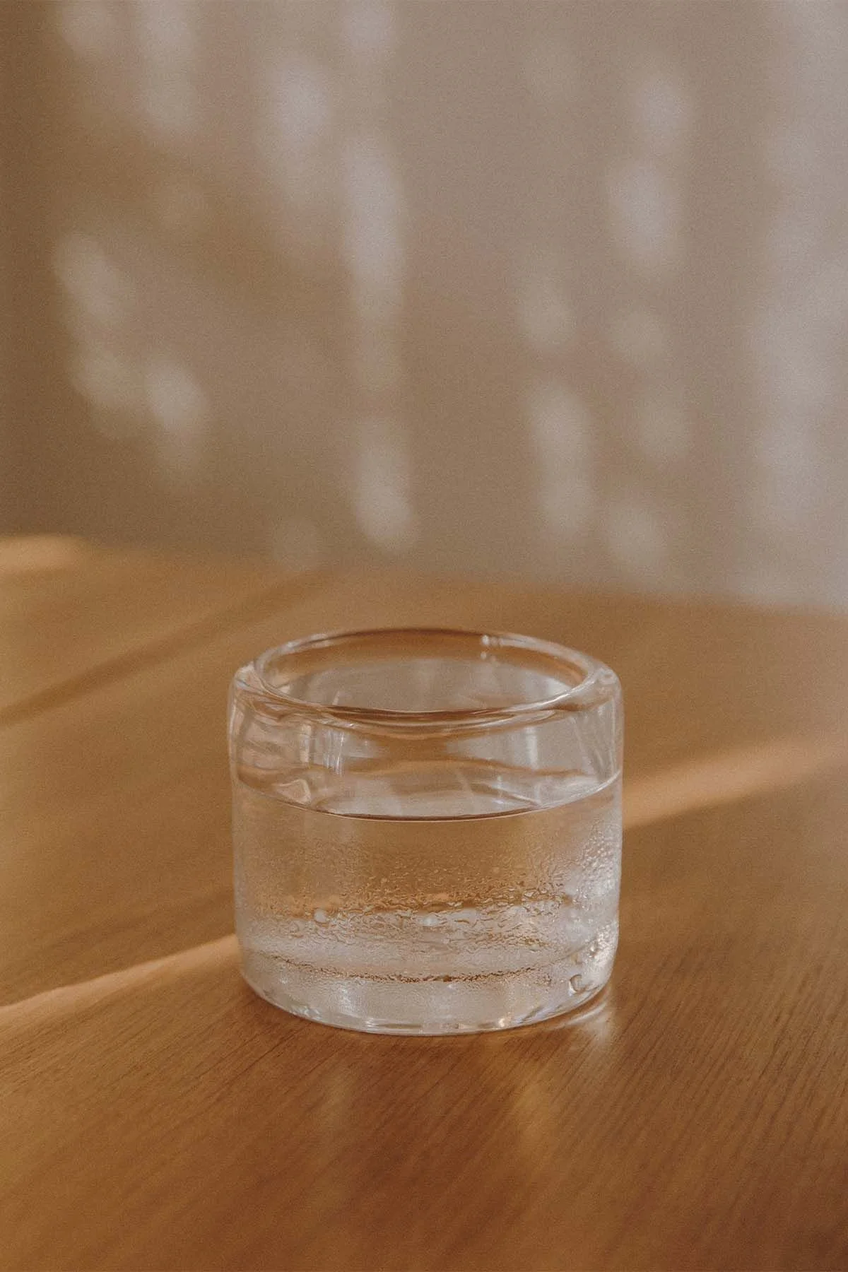 A small glass container filled with water on a wooden surface with reflections and a light-colored background.