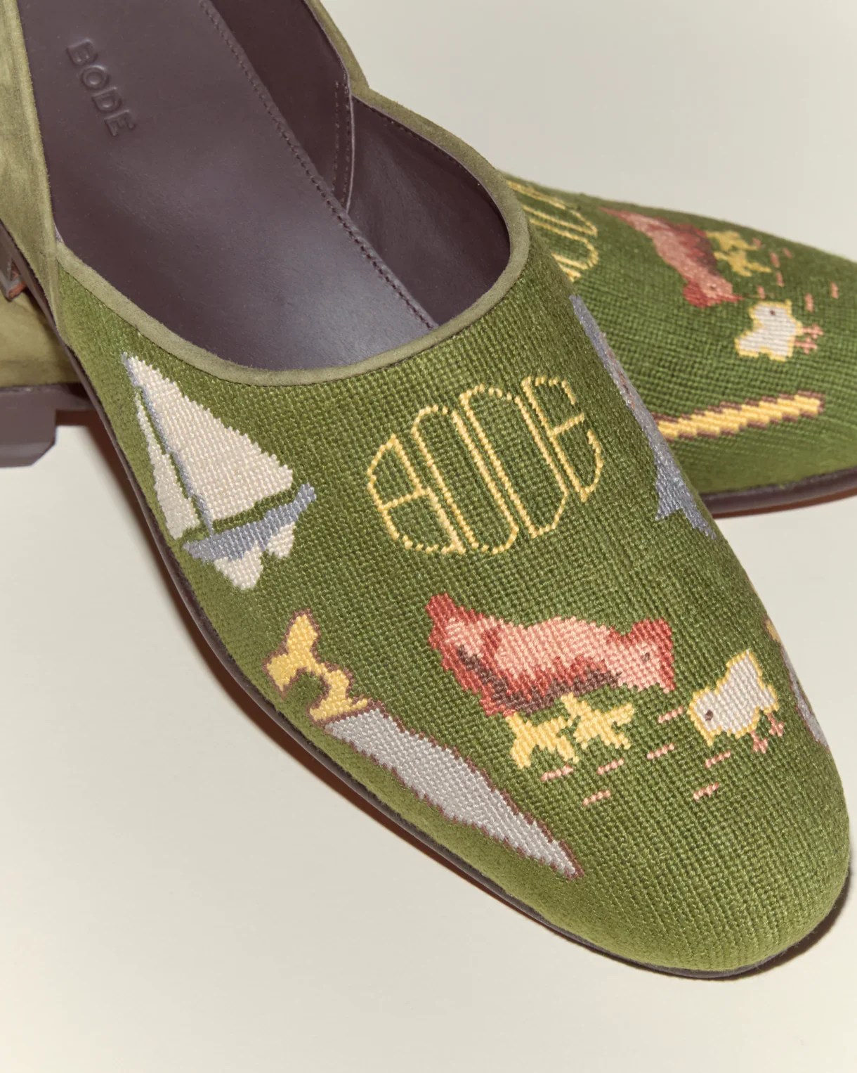 Green tapestry slip-on shoe with embroidered designs including a sailboat, the word "BOAT," a pig, a fish, and the word "BUG".