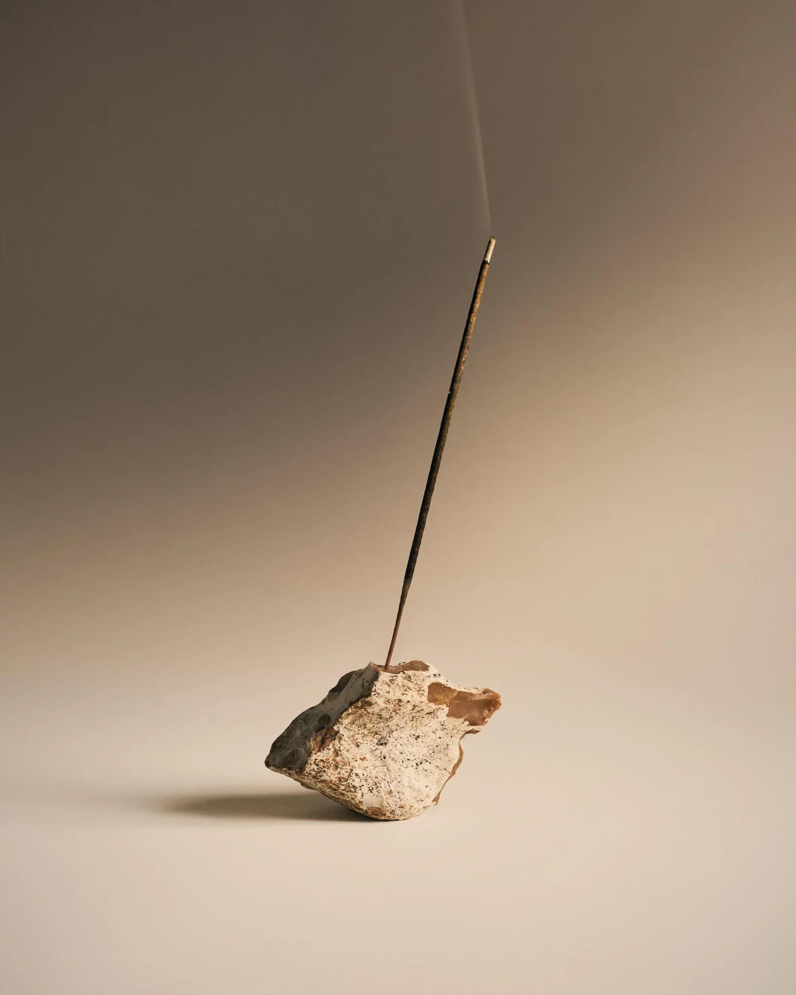 A piece of rock with an incense stick inserted into it on a plain background.