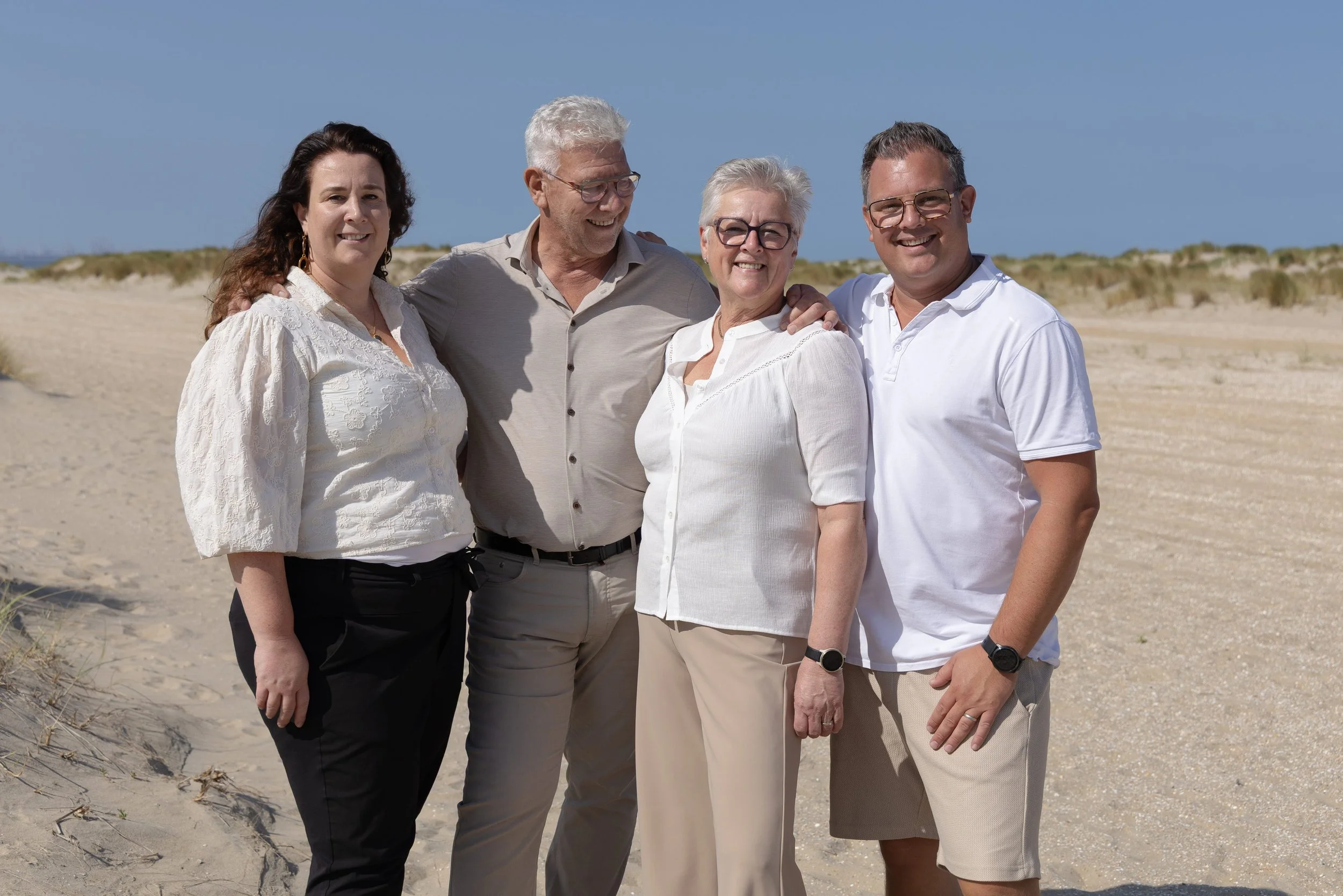 Vijf mensen die samen op het strand staan, glimlachen en elkaar omhelzen.
