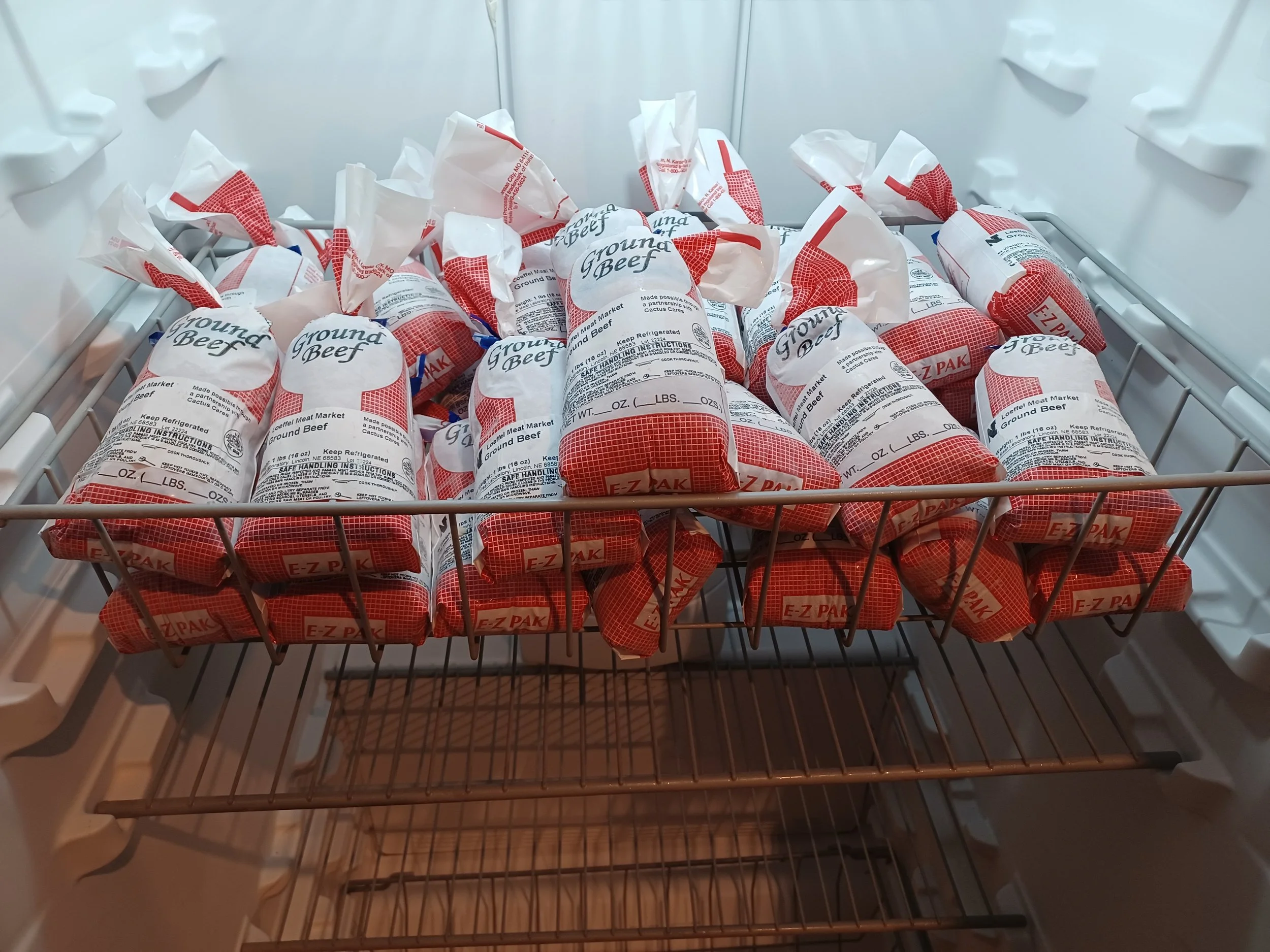 Open freezer drawer filled with packages of ground beef in white and red packaging.