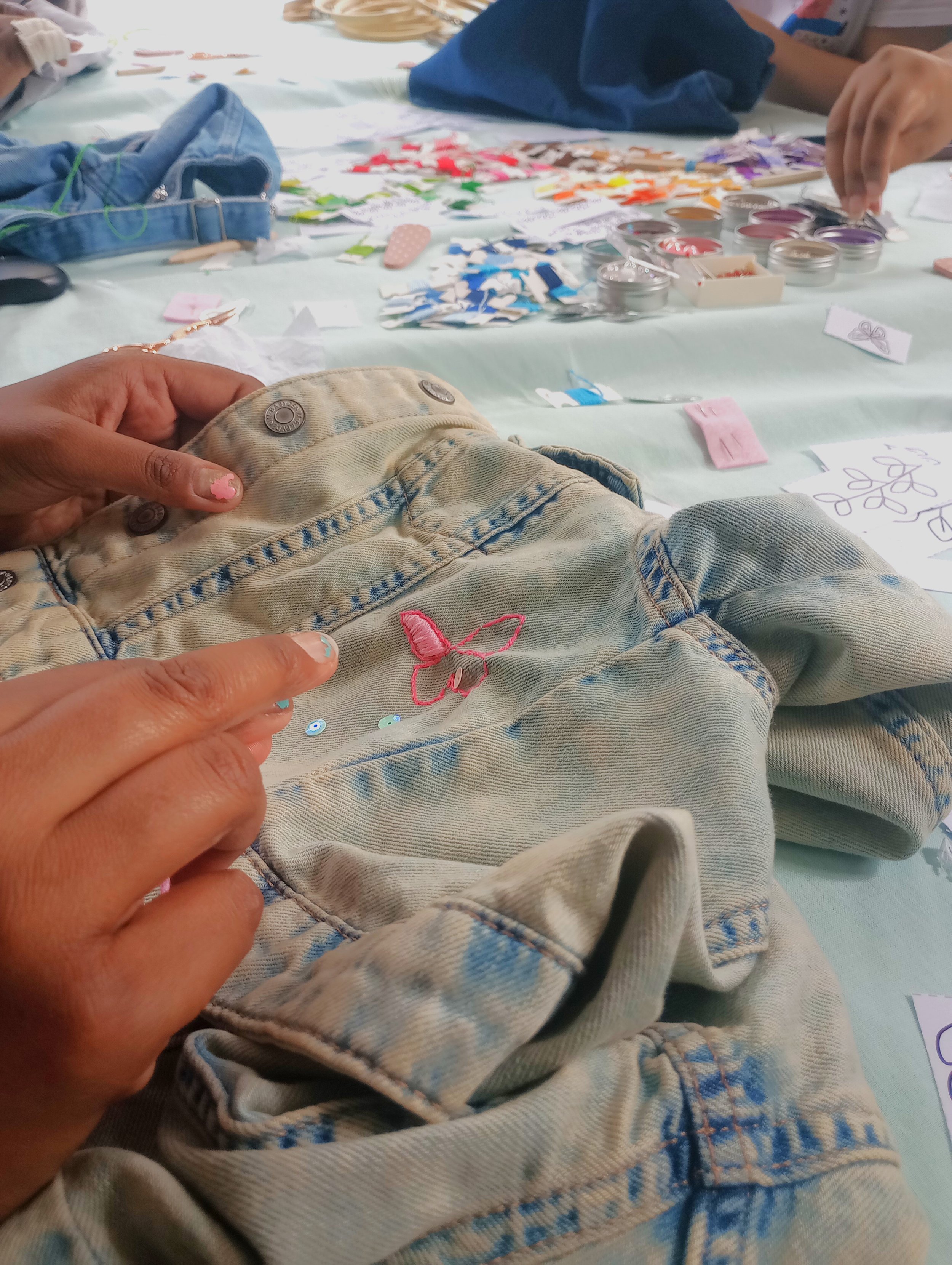 hands embroidering a butterfly on a denim jacket during a workshop