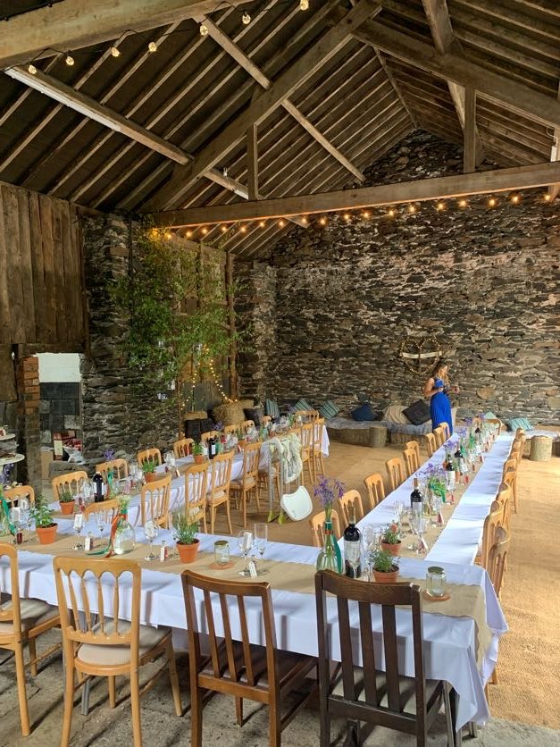 beautiful rustic welsh barn dressed for a wedding with long tables and fairy lights lining the beams