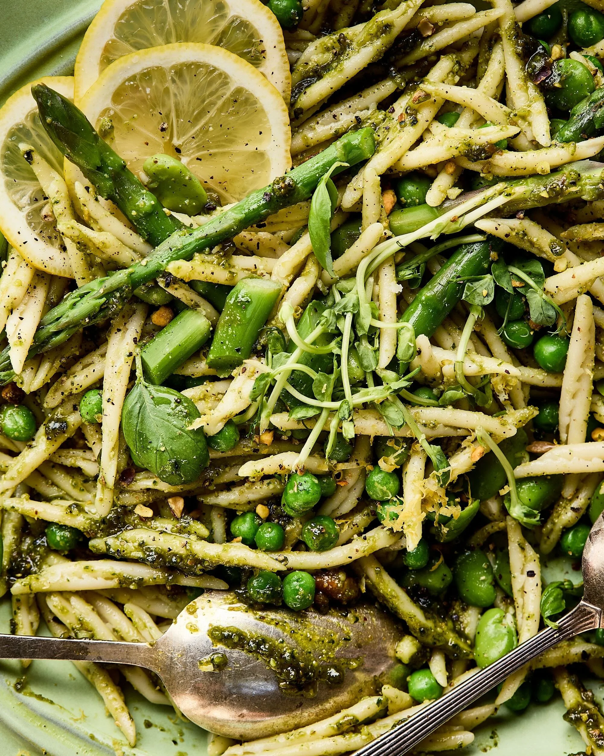 Close-up van trofie pasta al pesto genovese, frisse voorjaarsgroenten als asperges, tuinbonen en doperwten en citroen.