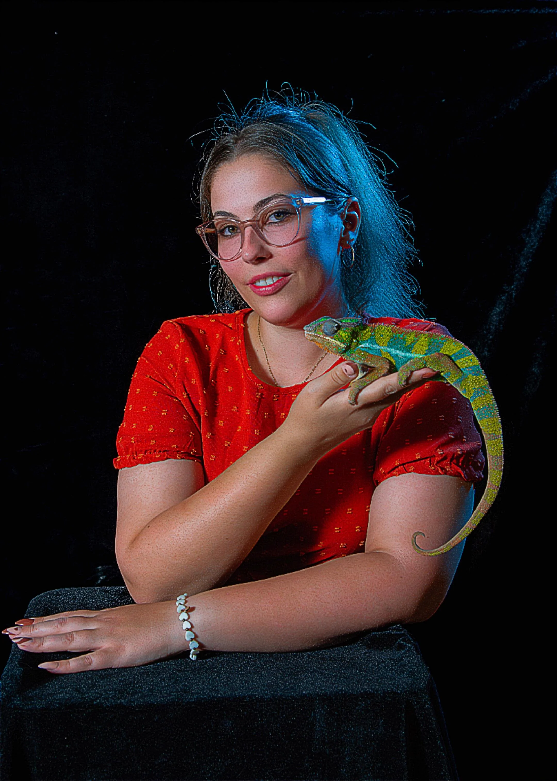 Eine Frau mit bräunlichen Haaren, Brille und rotem Kleid hält eine grüne Kalotte auf ihrer Hand, vor einem schwarzen Hintergrund.