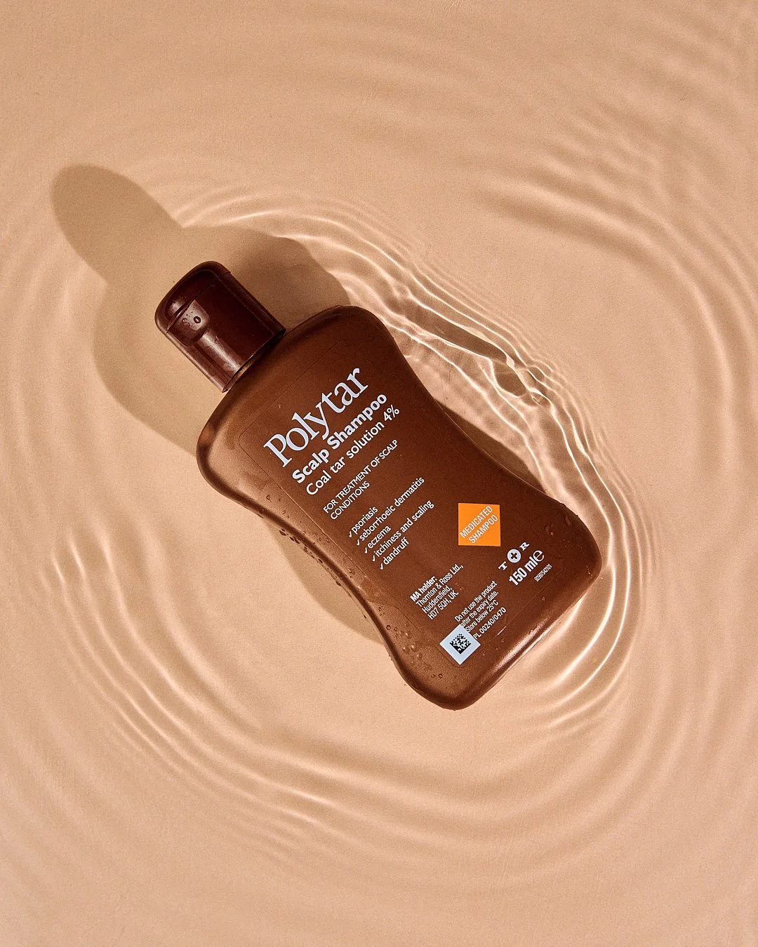 A brown bottle of Polytar Scalp Shampoo lying on a beige surface, with water ripples surrounding it.