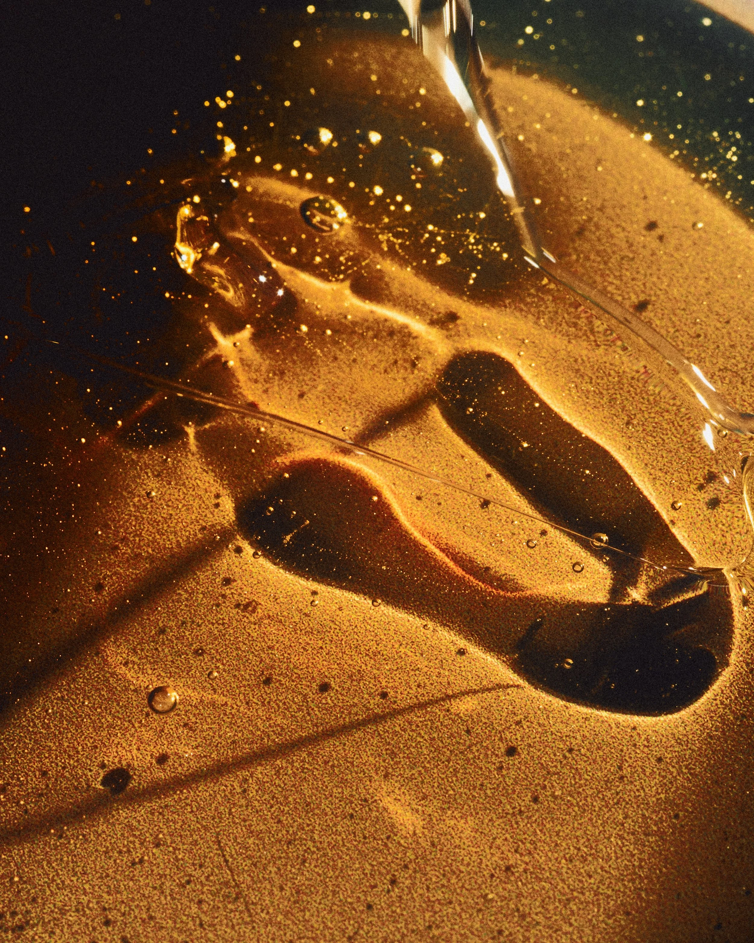 Close-up of a dark soda beverage with ice cubes and bubbles in a glass, placed on a reflective surface.