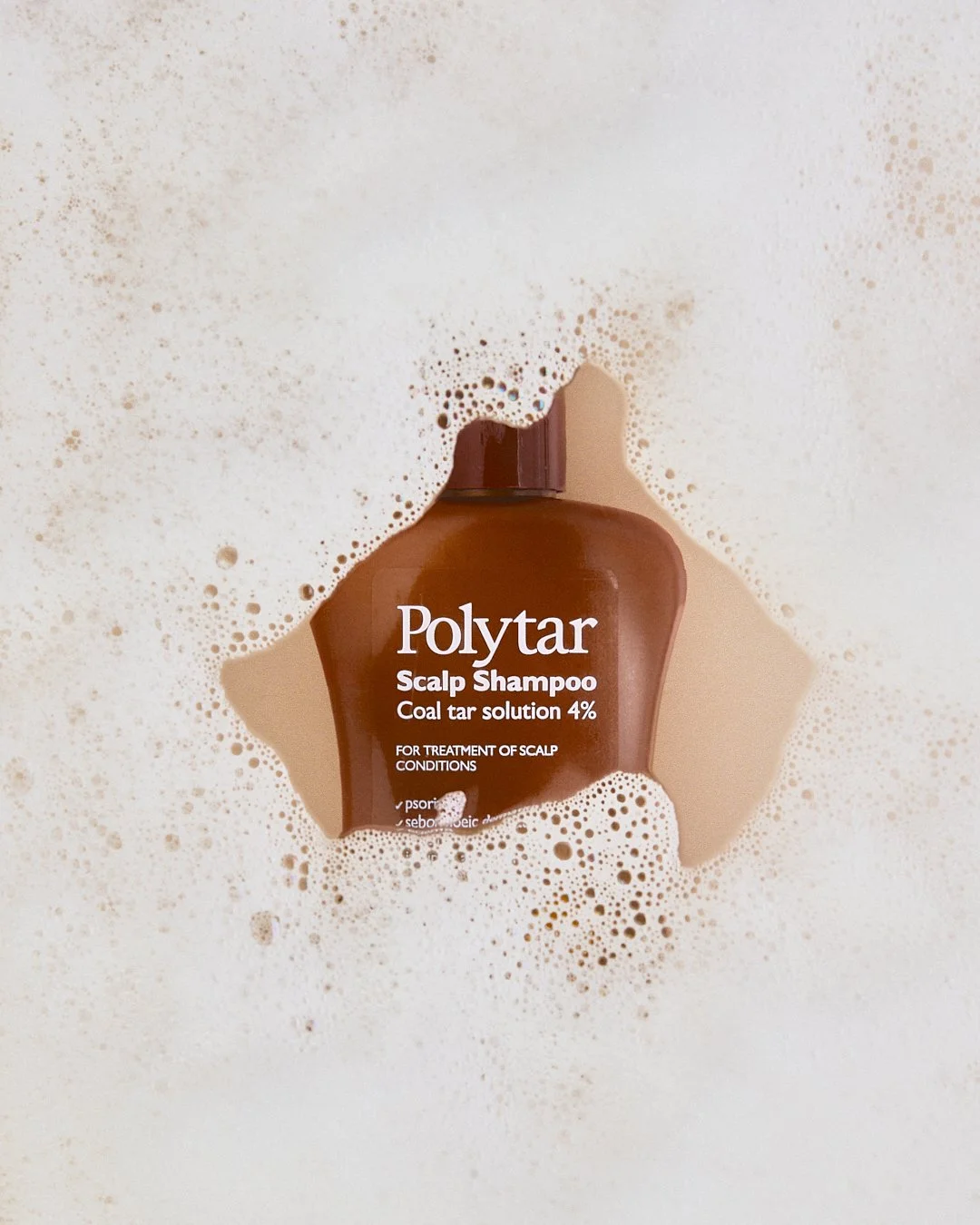 Bottle of Polytar Scalp Shampoo submerged in foamy bubbles.