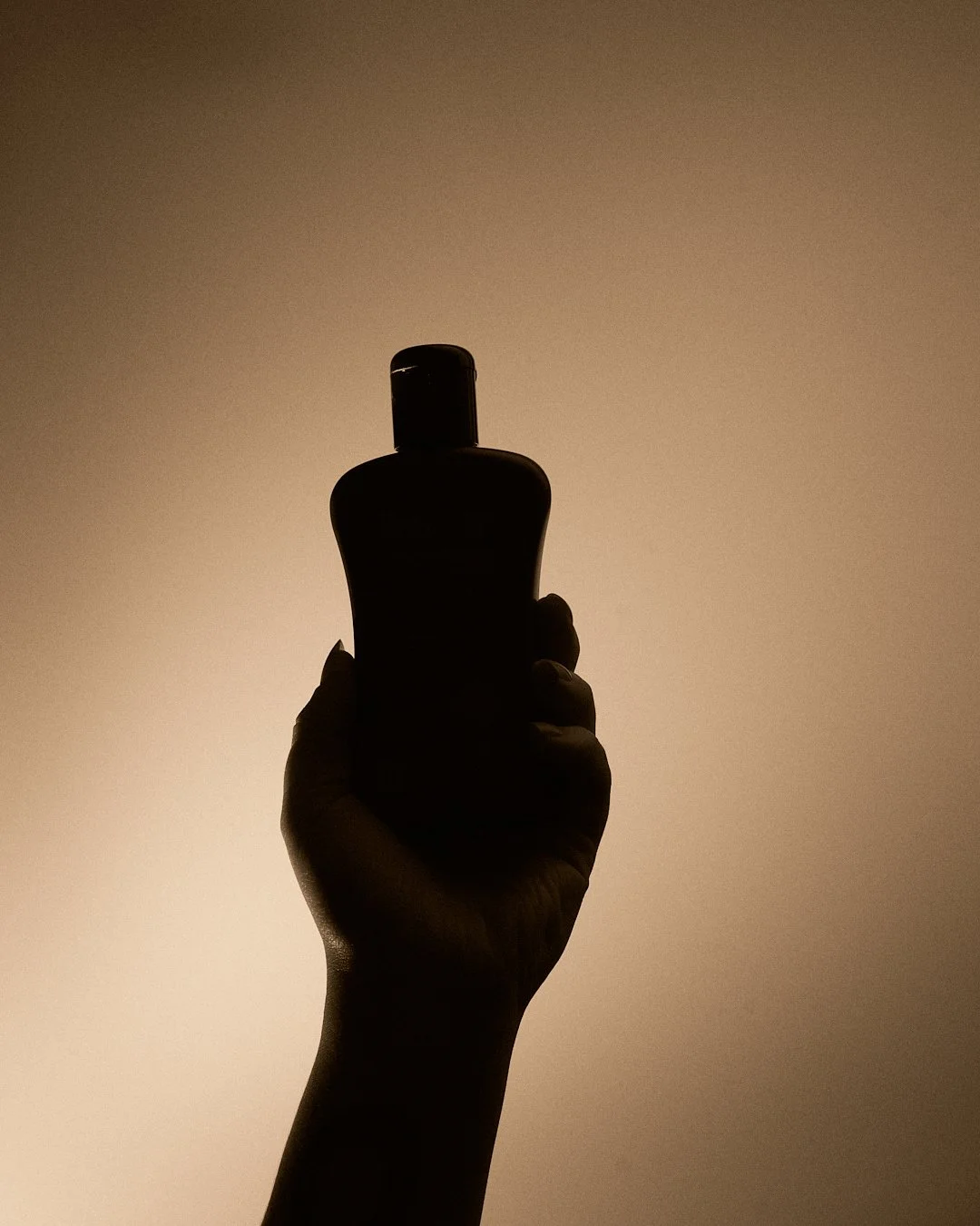 Silhouette of a hand holding a bottle against a plain background