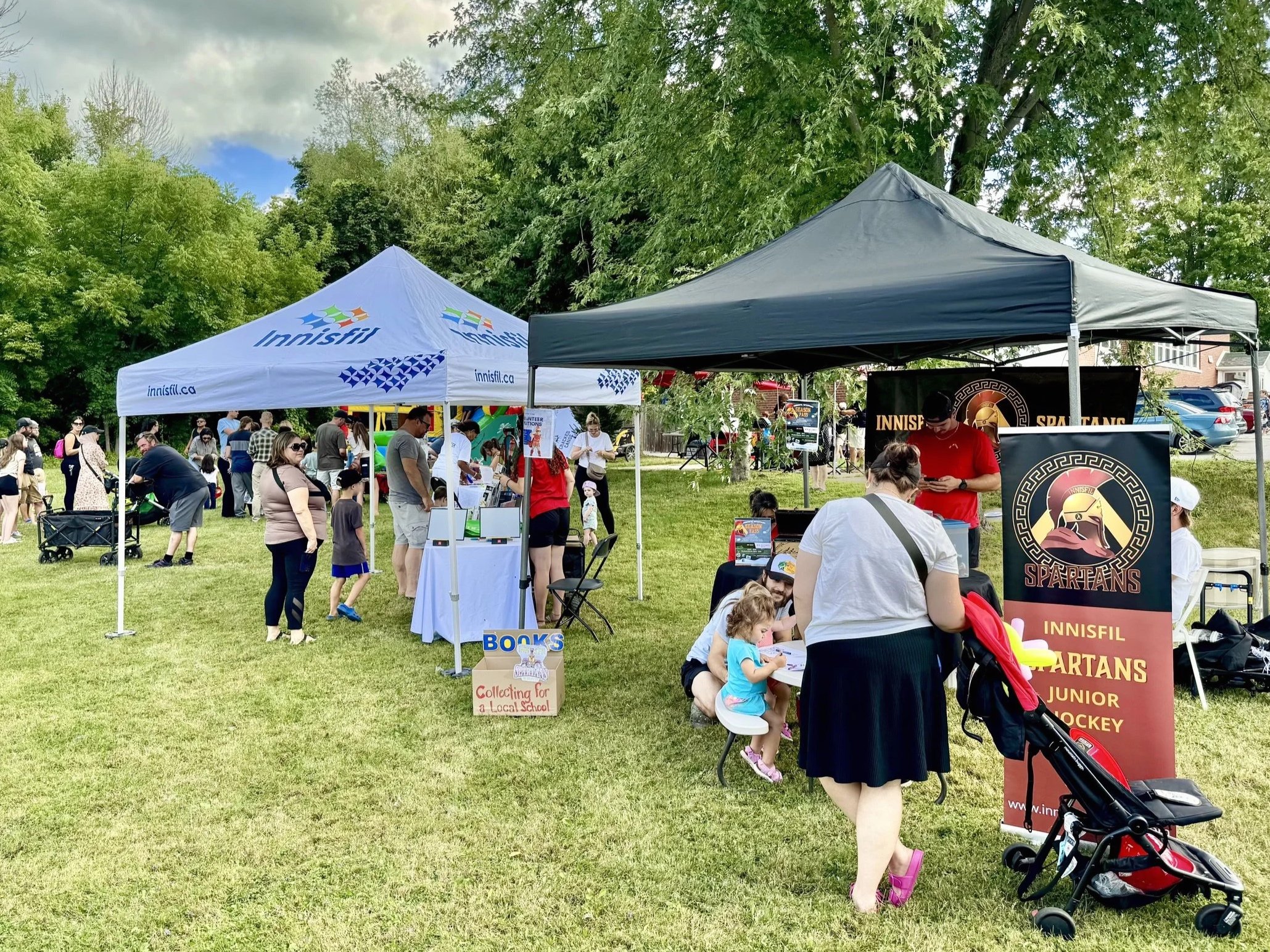 A community event outdoors in a park with tents and many people, including children, gathered for activities and booth displays.