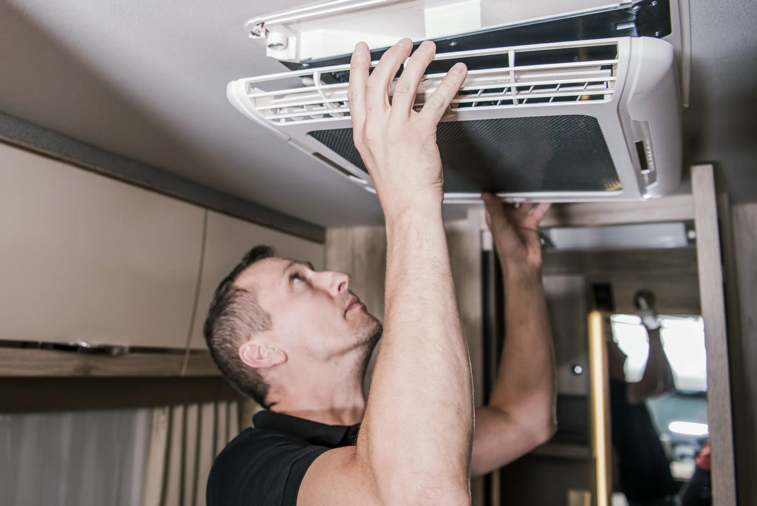 A man installing or repairing a wall-mounted air conditioning unit or vent in a room.