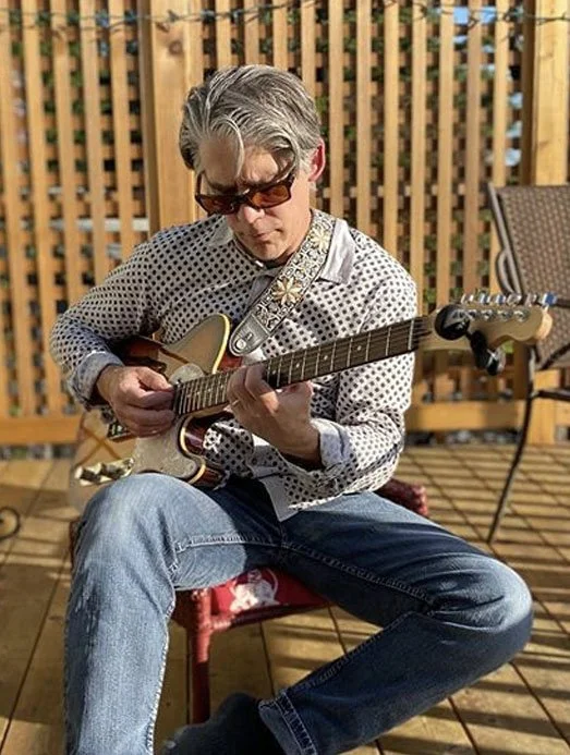 Creative Director Jeff Nichols playing a custom electric guitar on his deck in a relaxed, casual portrait.
