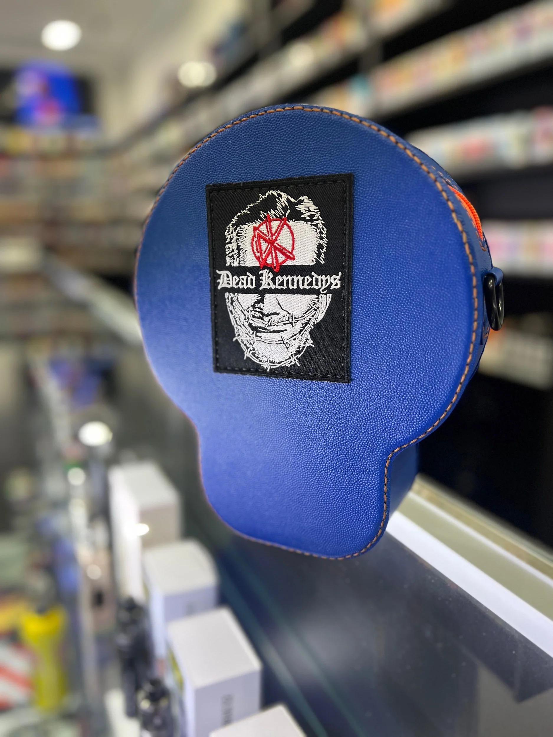 The reverse side of a circular electric blue leather skull pouch by Dead Punk Leather, featuring a sewn-on Dead Kennedys patch and vibrant orange hand-stitching.