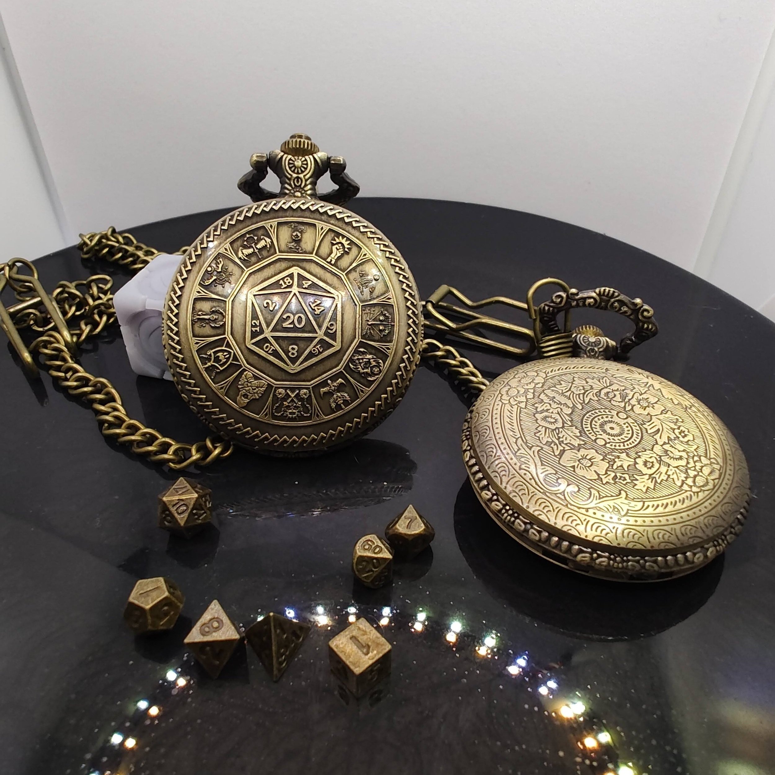 Bronze DnD pocket watches featuring a detailed D20 surrounded by class icons, displayed on a black surface alongside miniature metal RPG dice