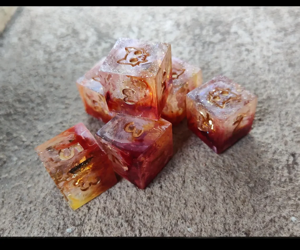 Six colorful resin dice with numbers etched in gold on a gray surface.