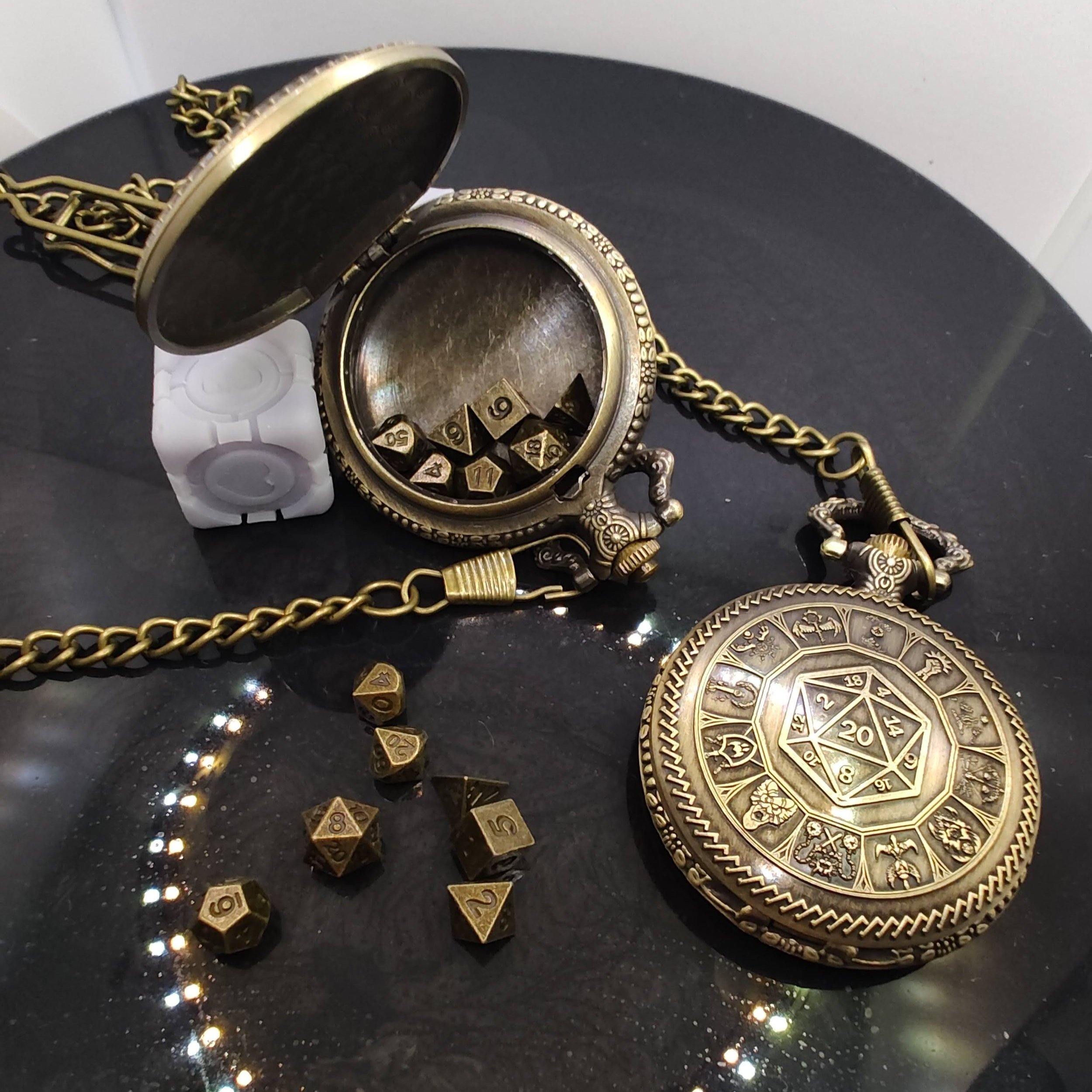One bronze DnD pocket watch opened to reveal a hidden compartment filled with mini metal dice, next to another closed watch showcasing a D20 and class symbols on a black backdrop