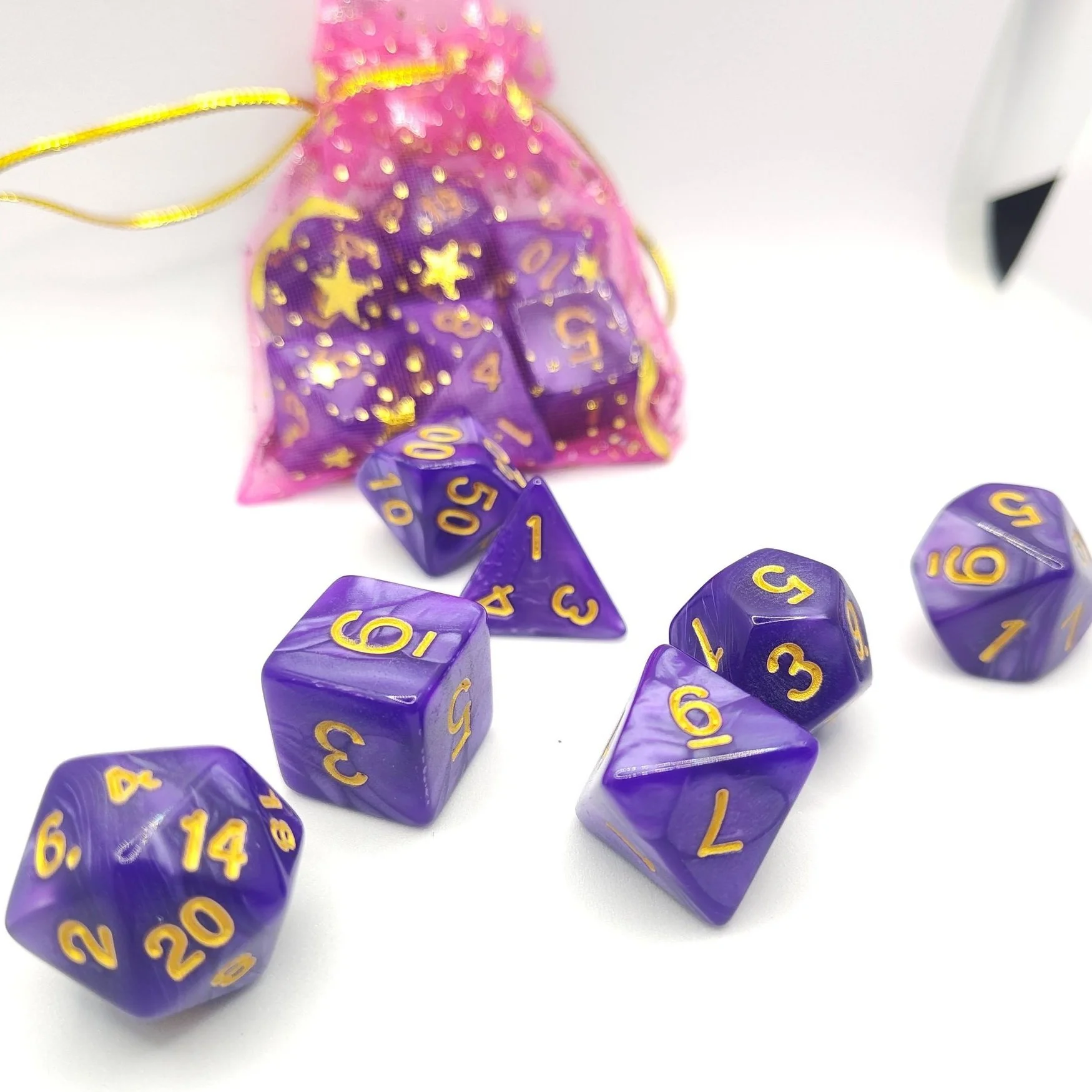 Bright amethyst-purple acrylic polyhedral dice set with gold numbering for DnD, Pathfinder, and other tabletop RPGs, displayed with a pink starry dice bag on a white background