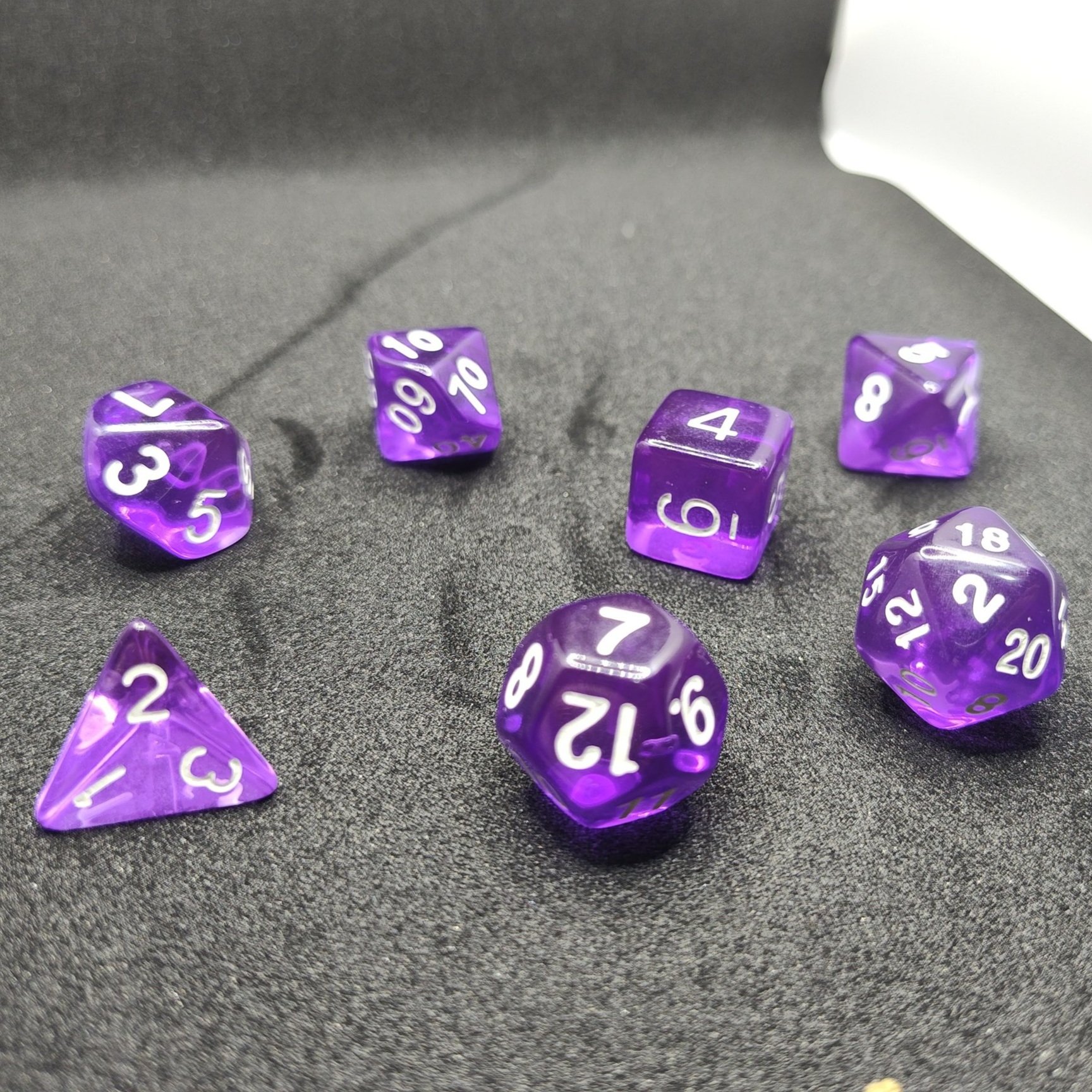 Seven purple acrylic dice with crisp white numbers, arranged on a black backdrop, ideal for tabletop RPGs