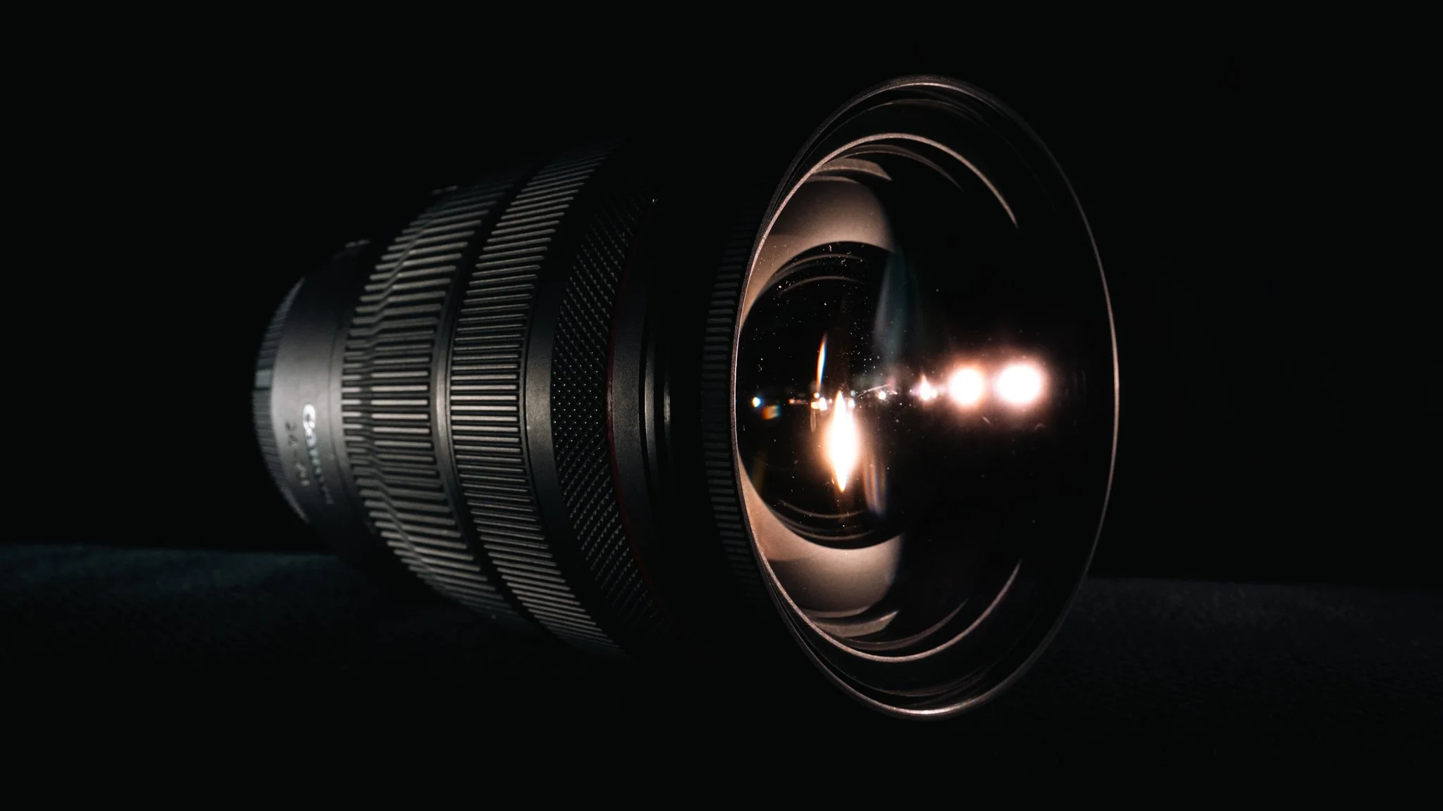 Close-up of a camera lens with reflections of lights in a dark background.