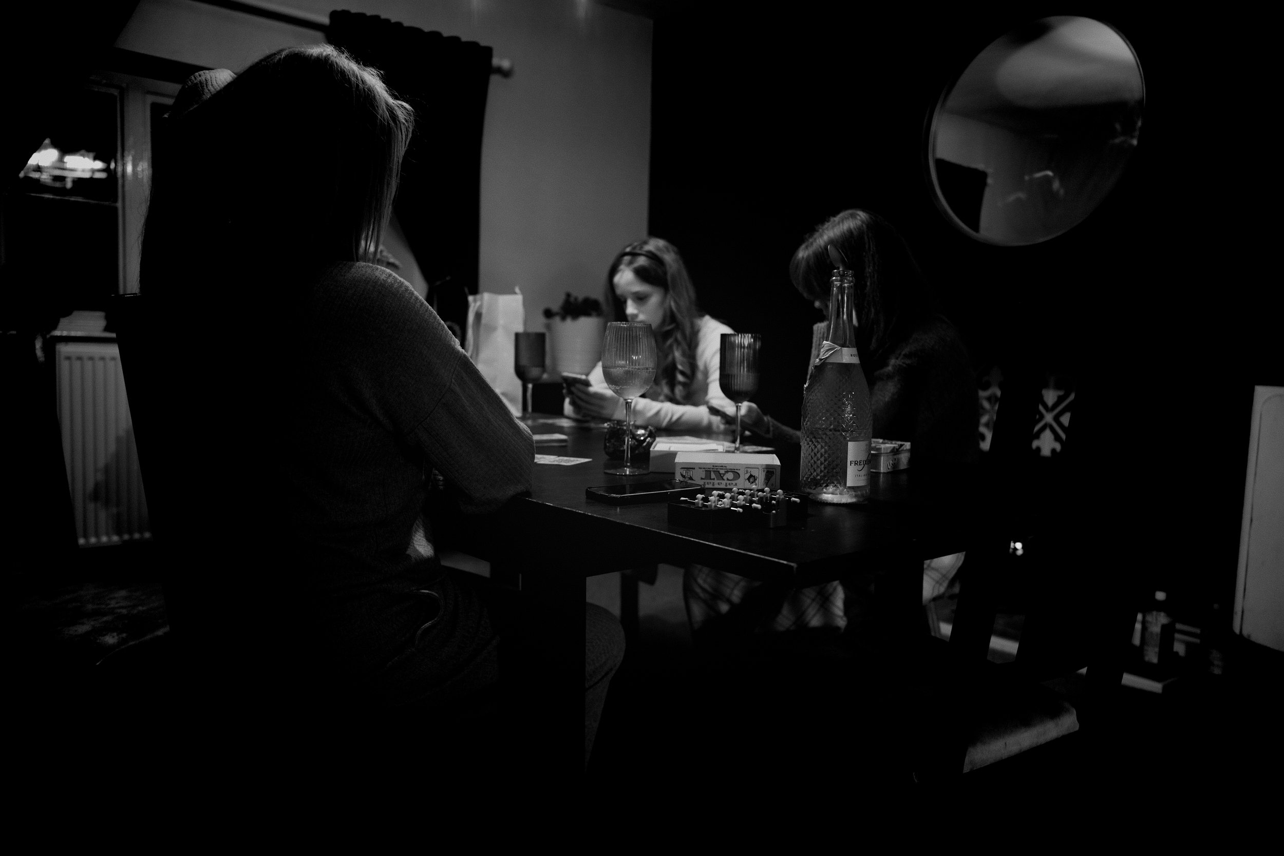 Four women sitting around a table playing a game, with drinks and snacks on the table, in a dimly lit room.