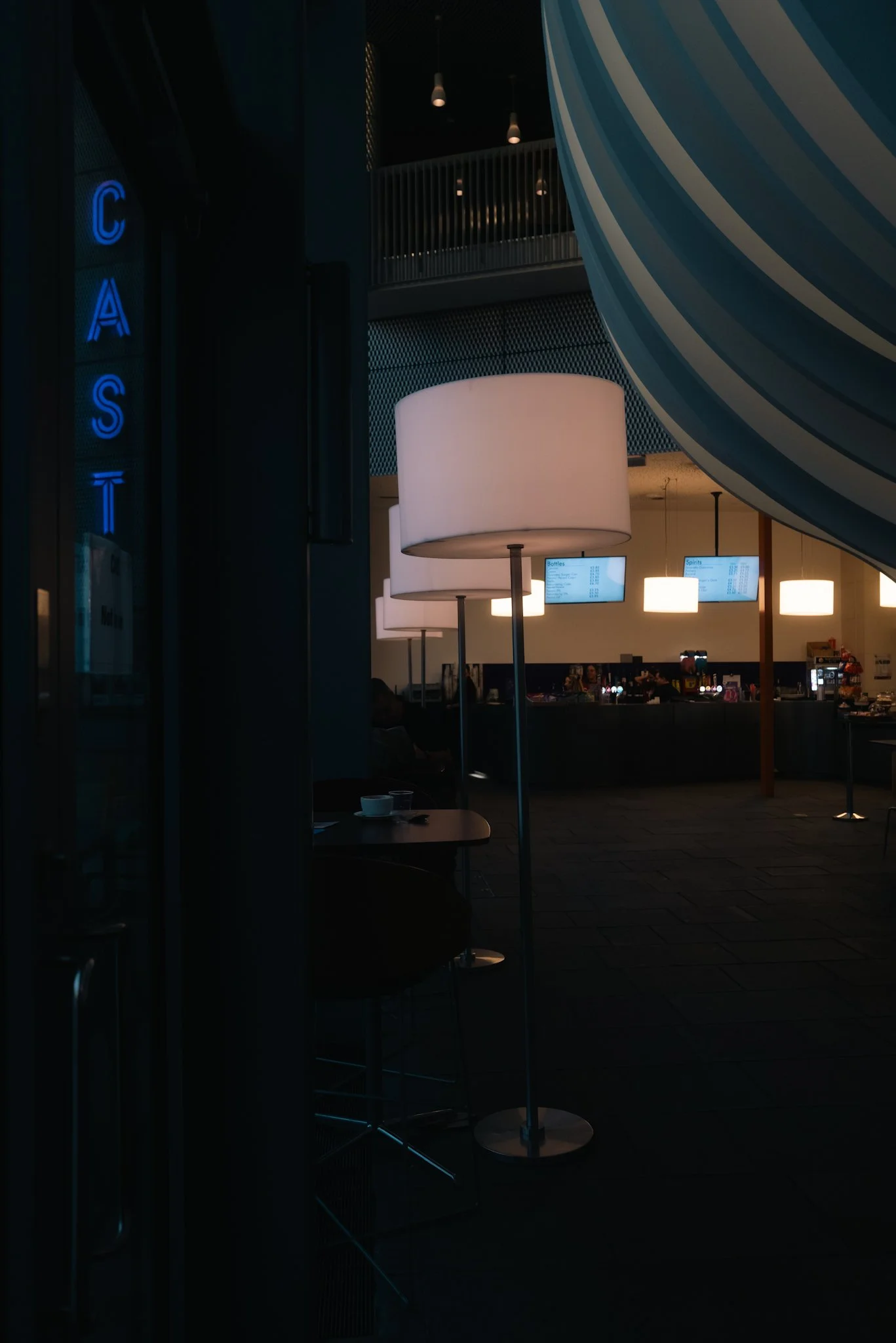 Interior of a dark restaurant or cafe with bright big lamps and digital menu screens in the background.