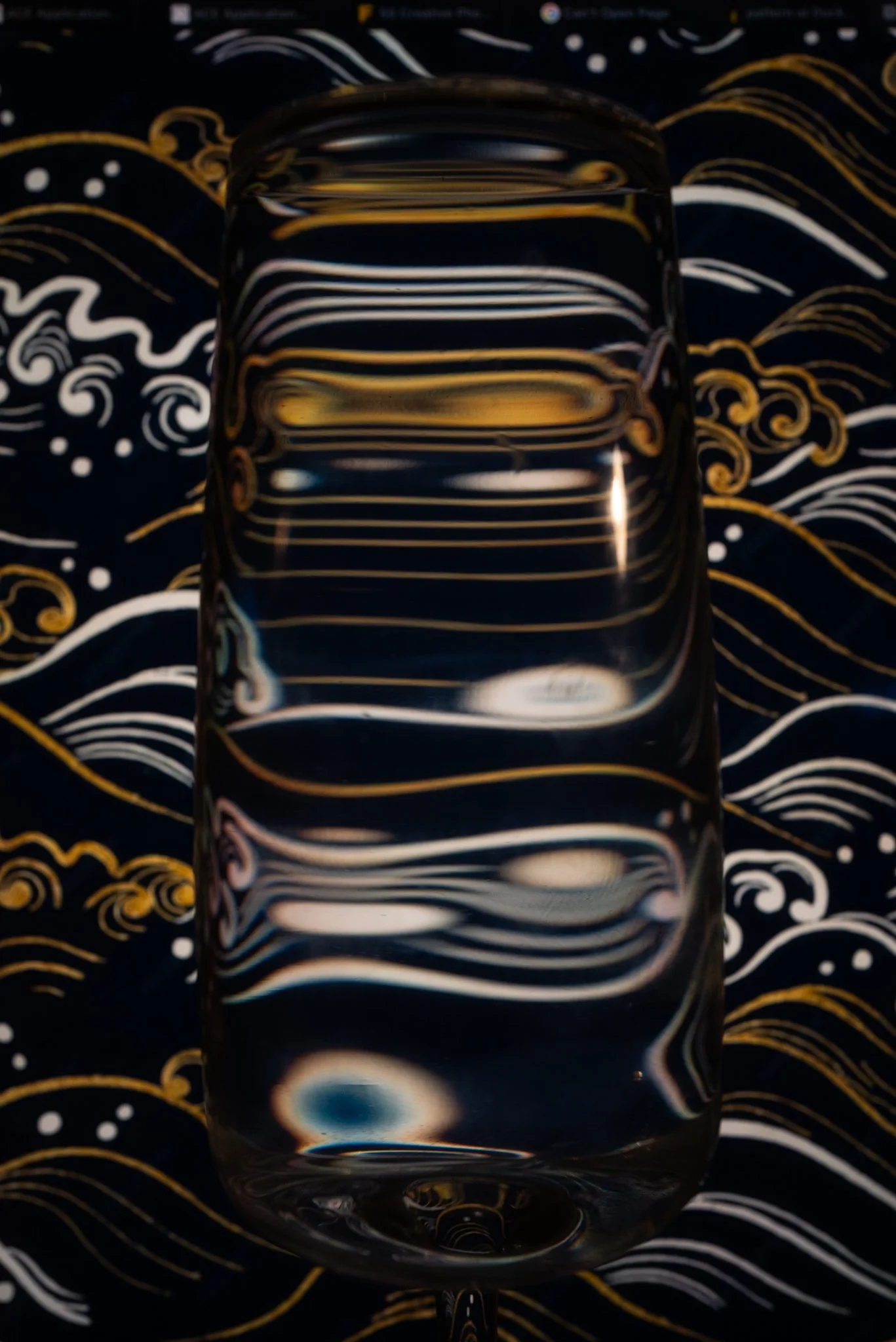A clear glass filled with water, placed on a dark background with intricate gold and white swirling patterns.