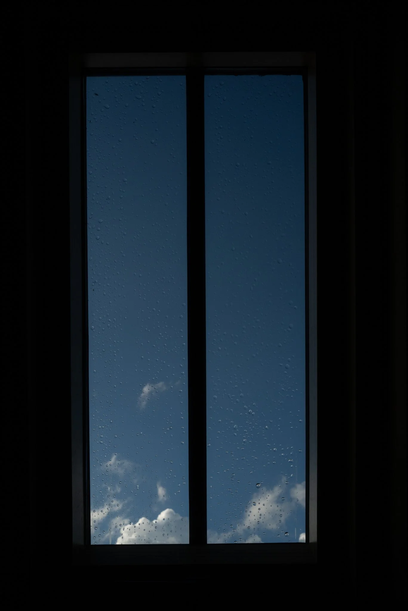 View of a blue sky with clouds through a rain-spattered window.