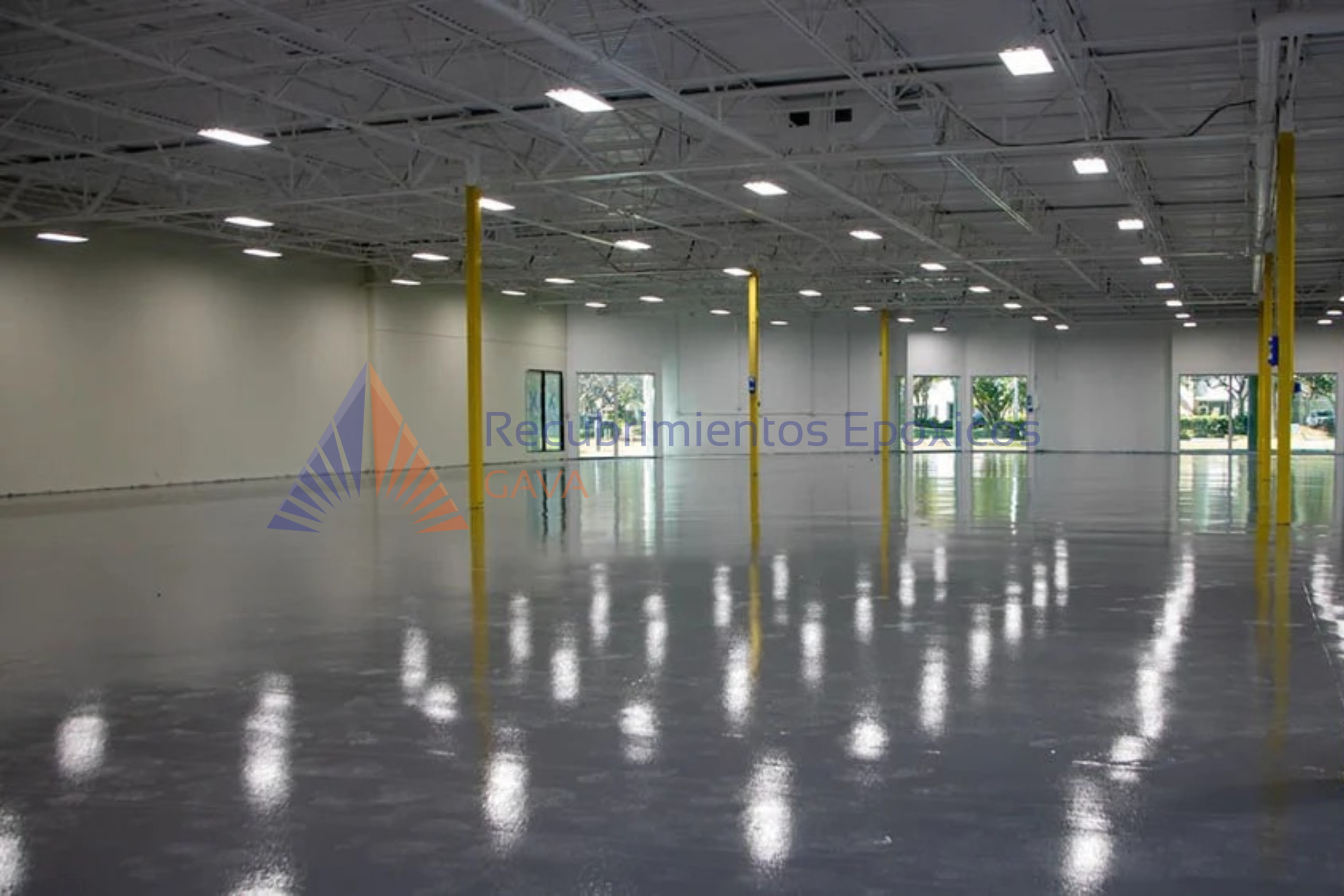 Interior de un almacén o espacio industrial con piso pulido, columnas amarillas y ventanas grandes que dejan entrar luz natural.