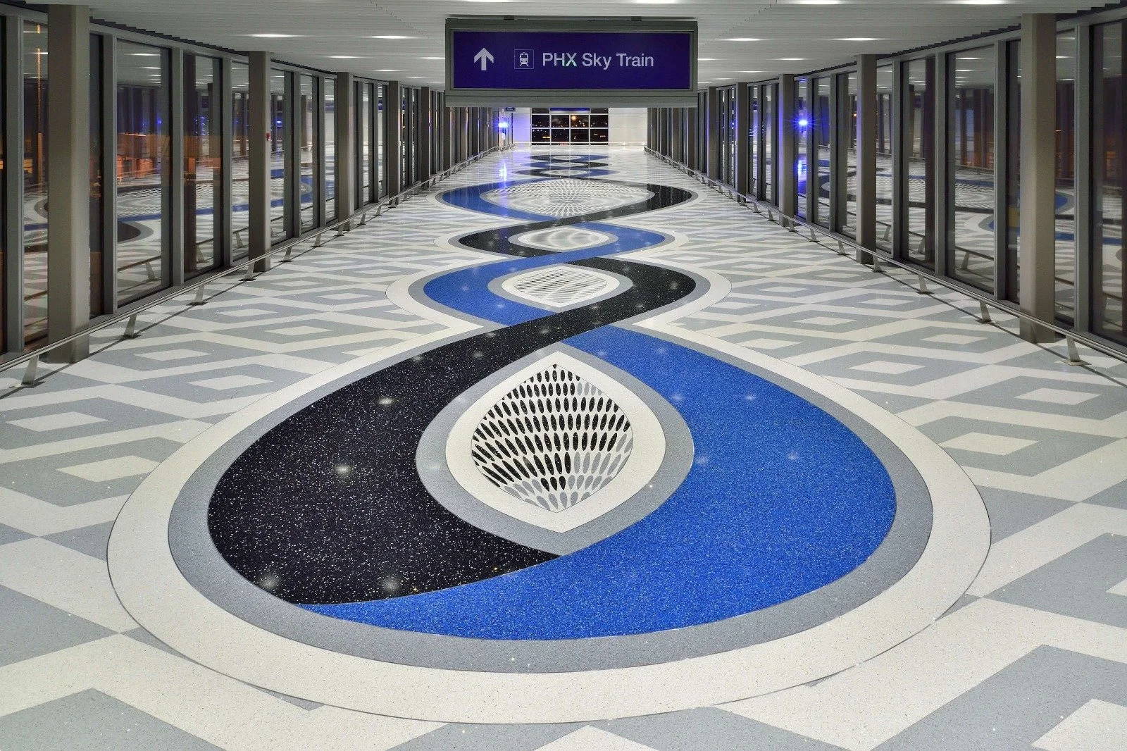 Pasillo del aeropuerto con un mosaico colorido en el piso y un cartel que indica dirección al 'PHX Sky Train'