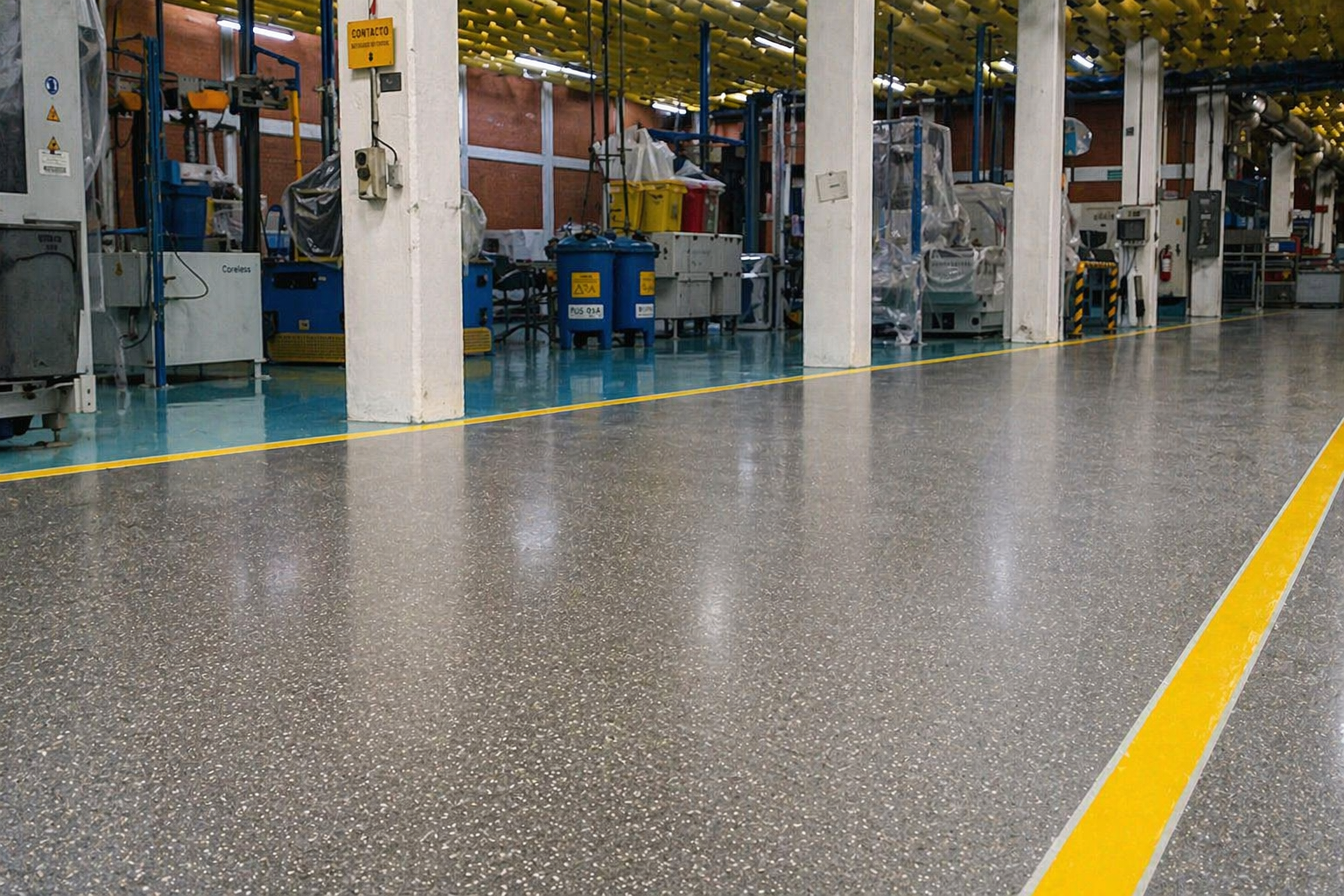 Interior de una fábrica con maquinaria y piso de concreto pulido, marcado con líneas amarillas para delimitar áreas de trabajo.