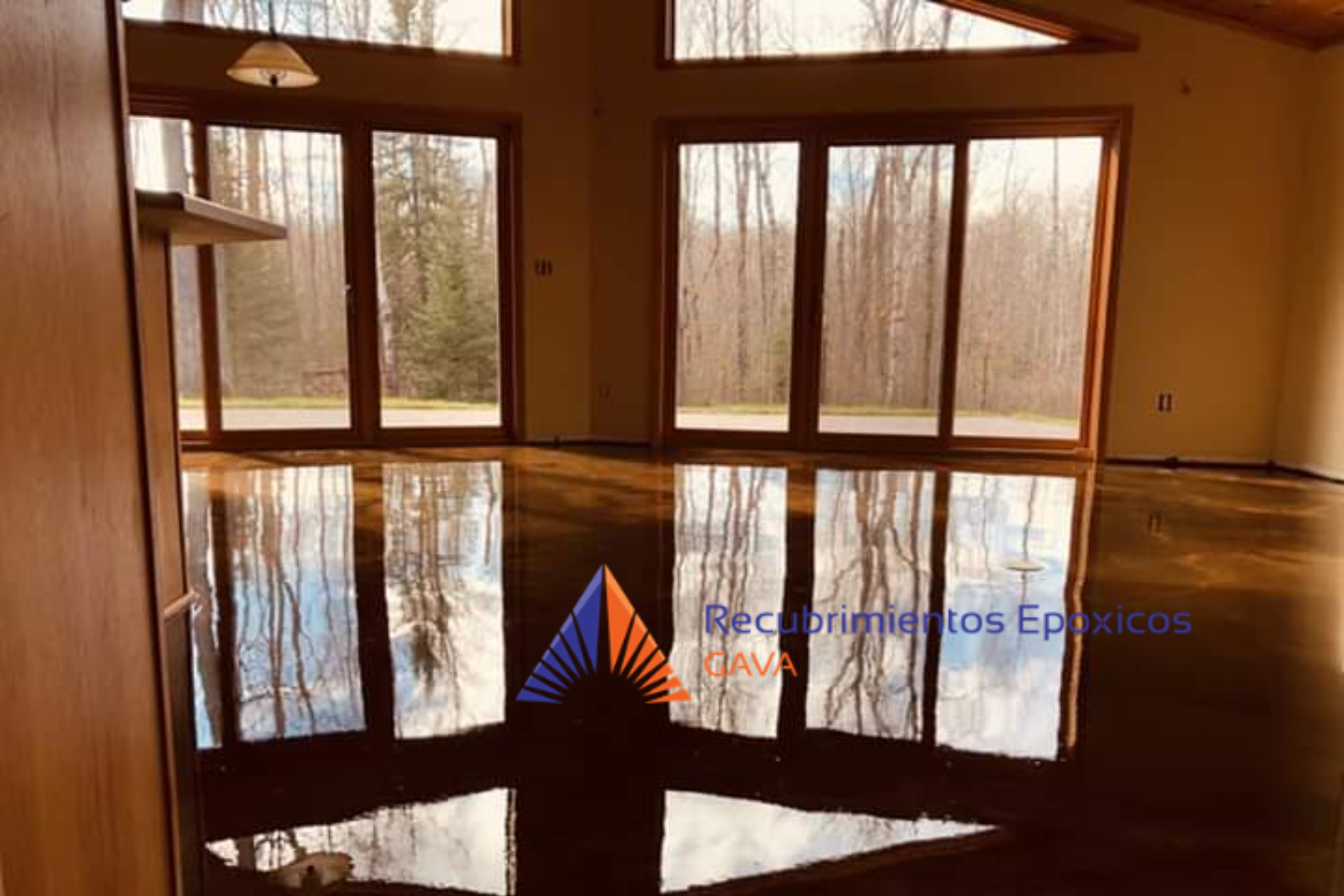 Interiores de una casa con paredes de color crema, pisos de madera pulida, y grandes ventanas que muestran un bosque exterior con árboles sin hojas.