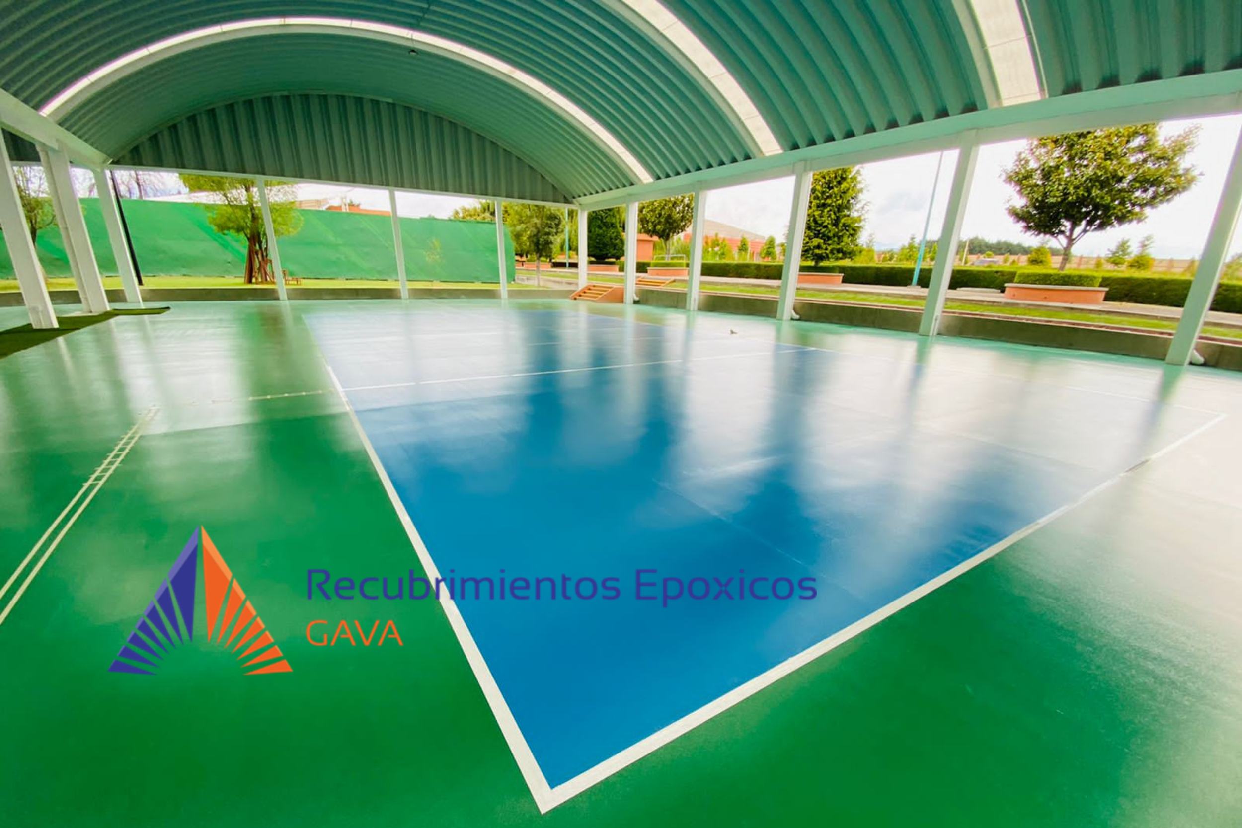 Pista de tenis bajo una estructura de techado de arco, con áreas verdes y árboles en el fondo, y logotipo de Recubrimientos Epóxico GAVA en la esquina inferior izquierda.