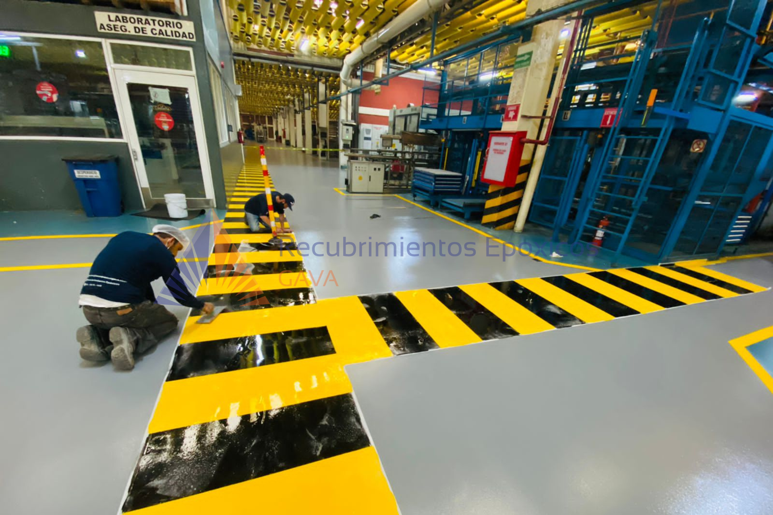 Personal trabajando en señalización de seguridad en el piso de una fábrica o planta industrial.