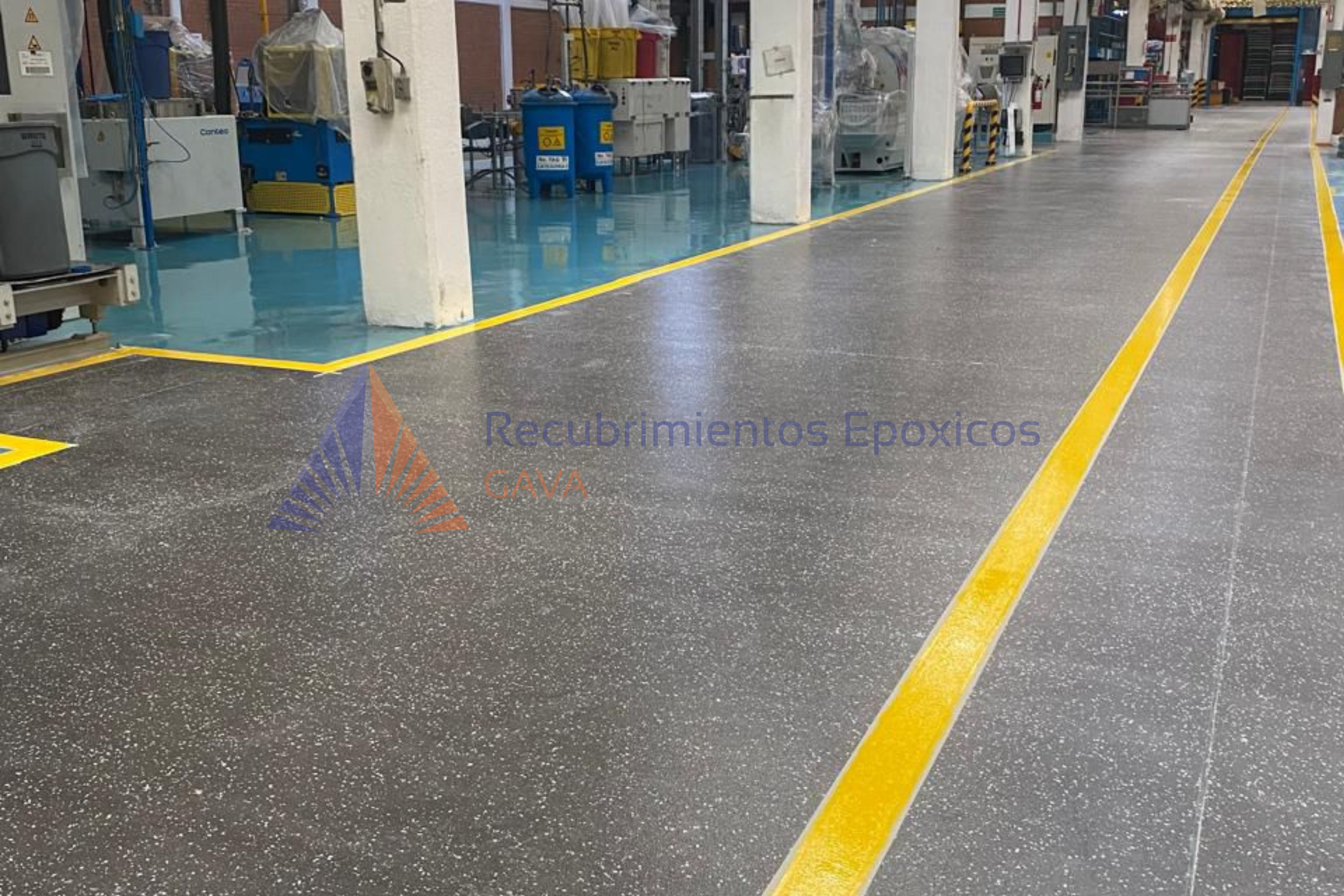 Piso de concreto con líneas amarillas para delimitar zonas, en un entorno industrial con equipo y maquinaria de fondo.
