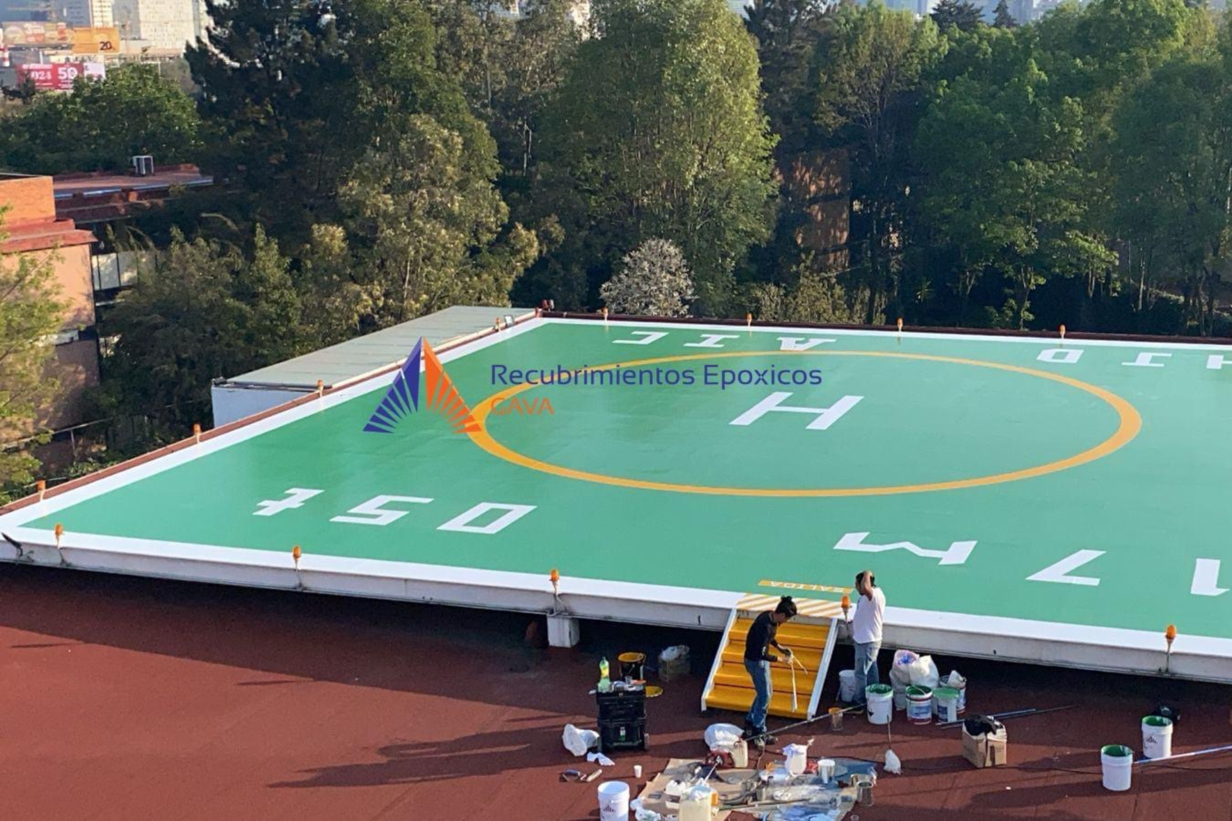 Trabajo en progreso de recubrimiento epóxico en una cancha de basketball, con herramientas y materiales repartidos en el suelo y trabajadores aplicando la pintura en la superficie.