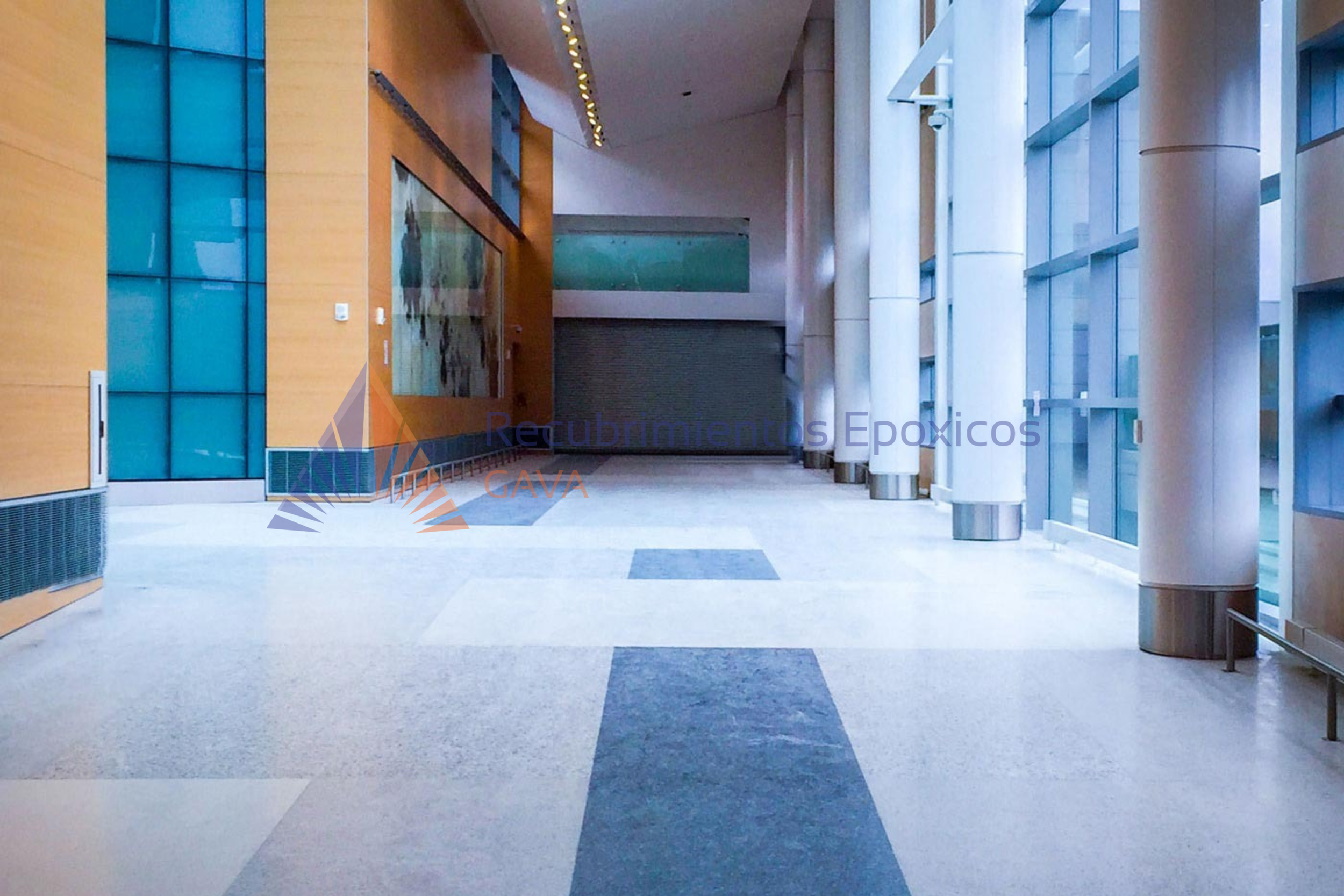 Interior de un edificio con paredes de colores amarillo y blanco, con columnas blancas y ventanas de vidrio que dejan entrar luz natural.
