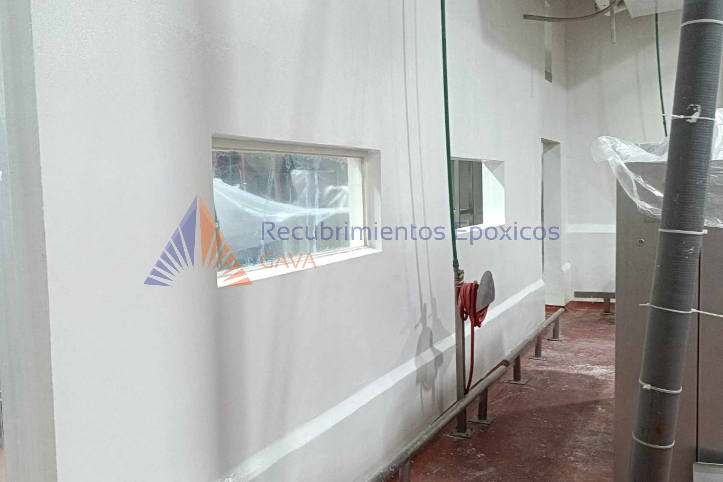 Pared blanca en una construcción con ventanas pequeñas, tuberías y un ventilador en el techo, en proceso de recubrimiento epóxico. Logo y texto de Recubrimientos Epóxicos GAVA en la parte inferior.