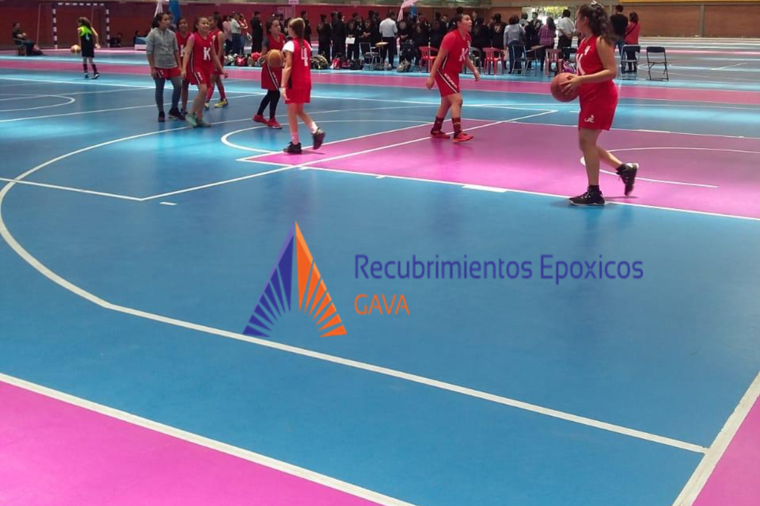 Grupo de niñas en una cancha de baloncesto, algunas conuniforme rojo, practicando y jugando. En el fondo, personas observando y un banner que dice 'Recubrimientos Epóxicos GAVA'.