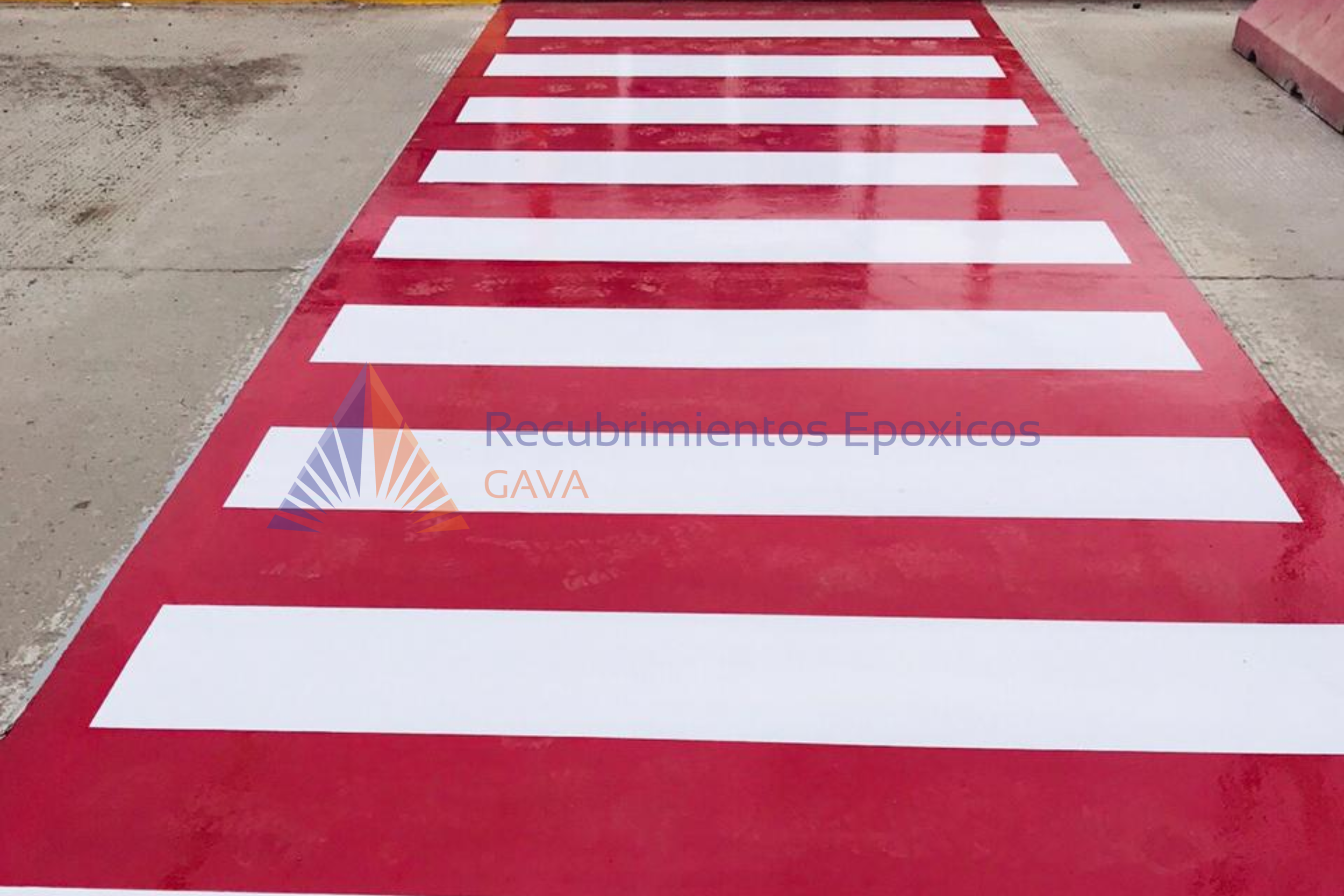 Paso peatonal pintado en la calle, de color rojo con franjas blancas.