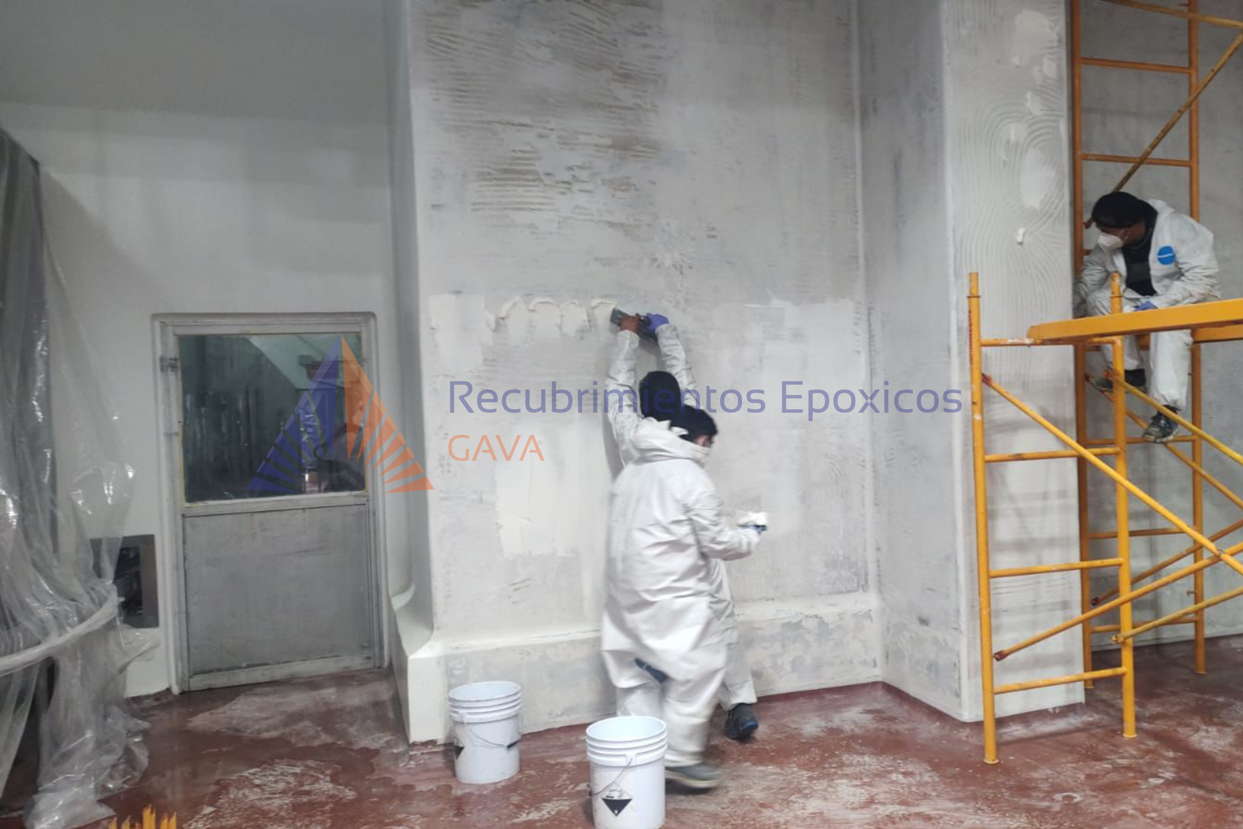 Dos personas trabajando en la aplicación de recubrimiento epóxico en una pared interior, con escaleras y cubetas de pintura en el lugar.