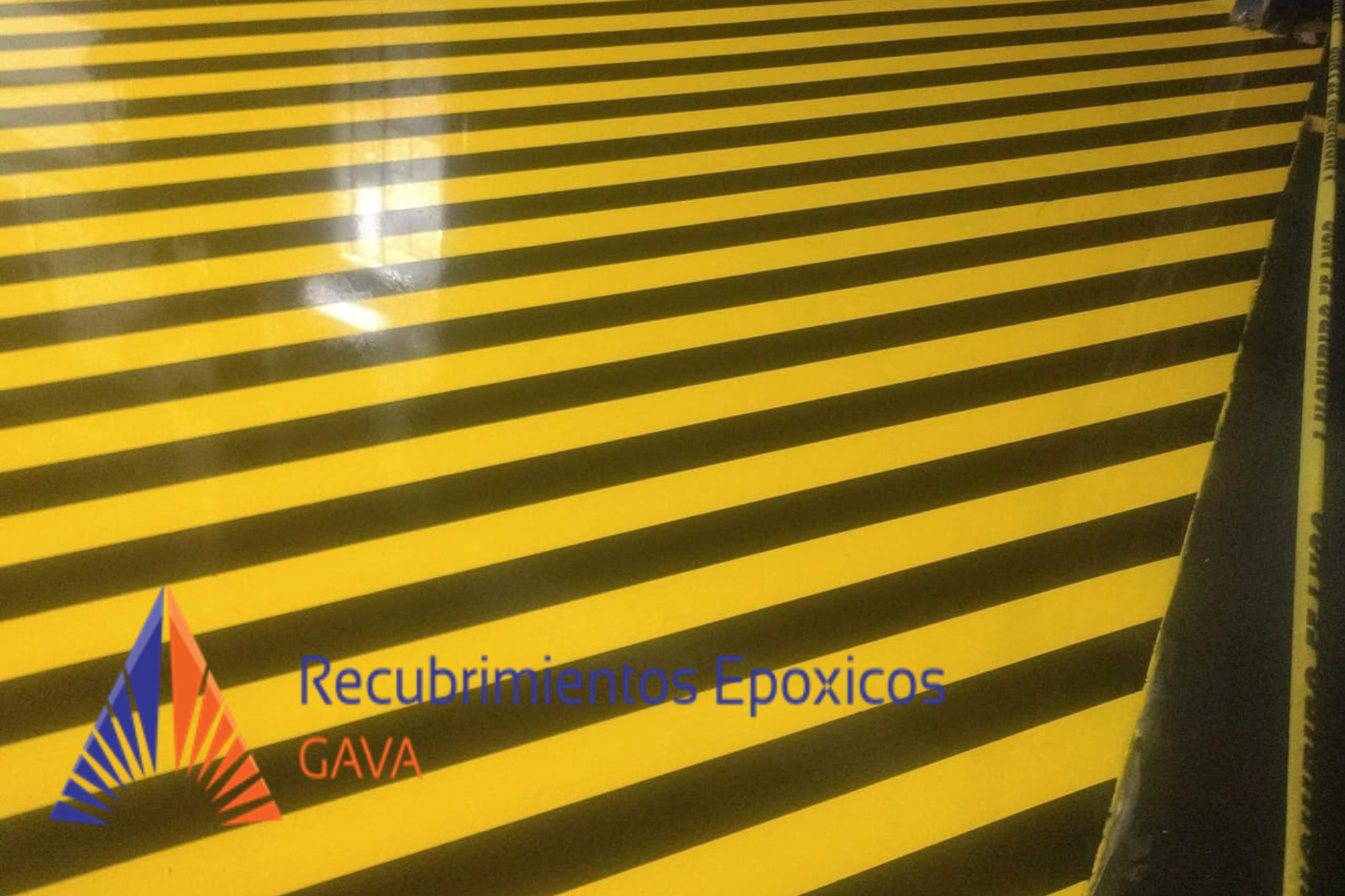 superficie de piso con líneas negras y amarillas de advertencia, con texto en la parte inferior que dice "Recubrimientos Epóxicos" y un logotipo de colores