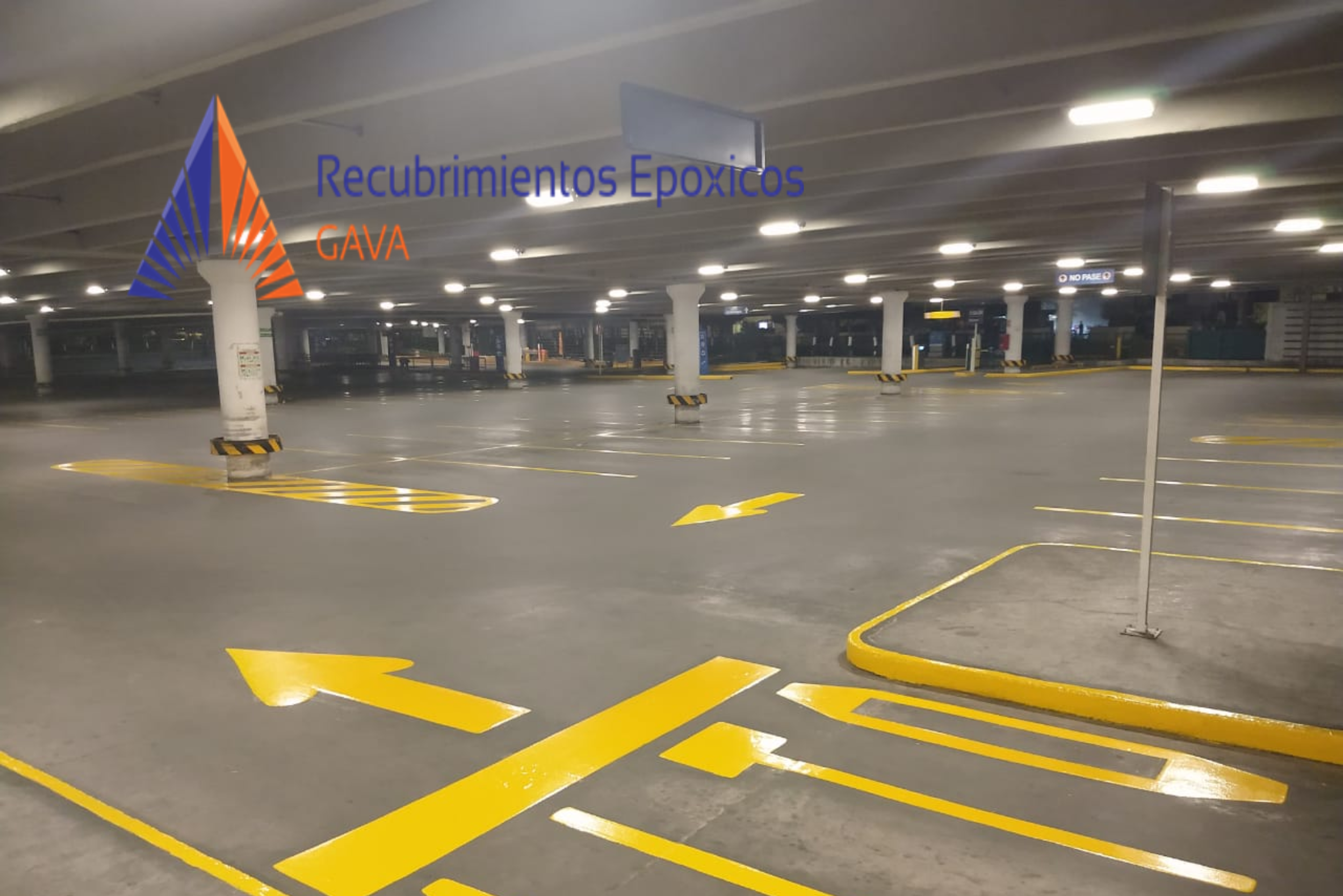 Estacionamiento subterráneo con señalización en amarillo para conducir y zonas vacías. Logo y texto en la esquina izquierda que dice 'Recubrimientos Epóxicos GAVA'.