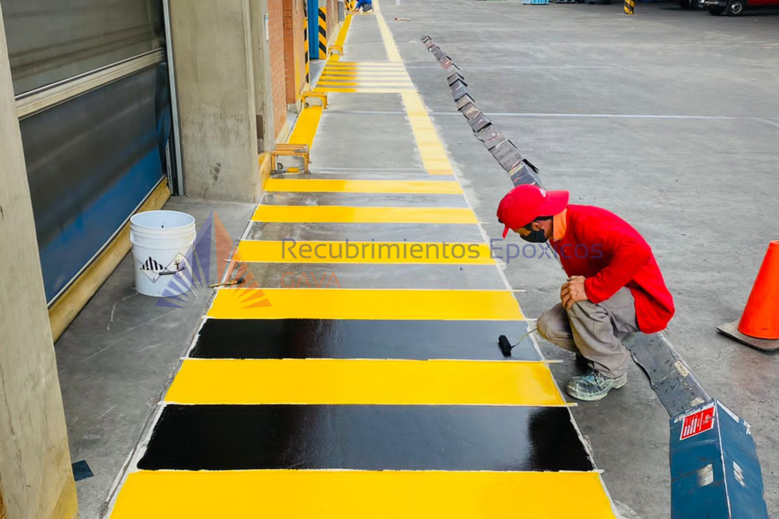 Persona pintando líneas amarillas y negras en el suelo de un estacionamiento.