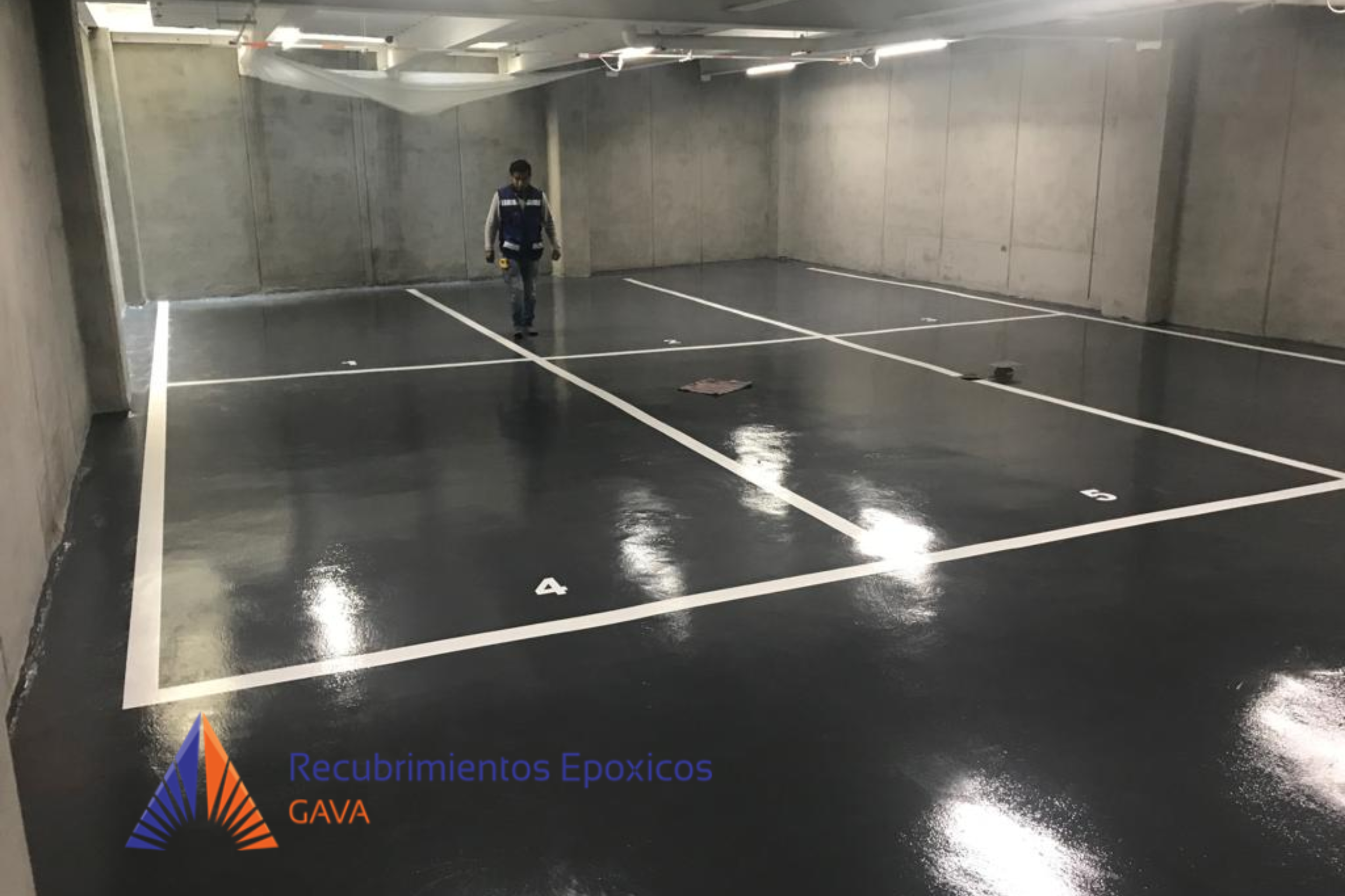 Estacionamiento con líneas blancas y un solo automóvil estacionado, en un espacio cerrado con paredes de concreto, una persona con mascarilla y uniforme trabaja en el piso, y en la esquina inferior izquierda hay un logo que dice Recubrimientos Epóxic