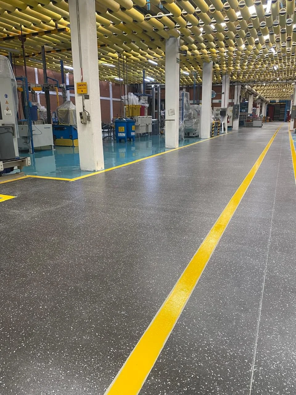 Interior de una fábrica o planta industrial con maquinaria y líneas de marcado amarillo en el suelo.