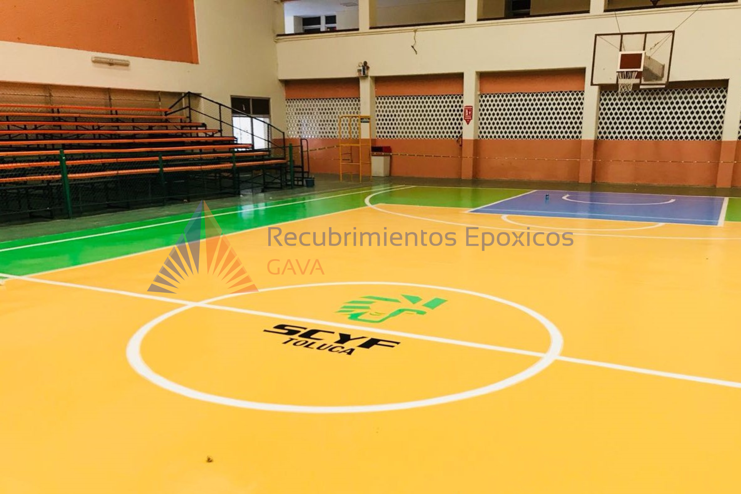 Pista de baloncesto en una cancha cubierta con pisos en colores azul, verde y amarillo, con señalización y logotipos de la marca Sky, y un área de bleachers al lado izquierdo. En el fondo, paredes con protección de paredes epóxicas y una portería de 