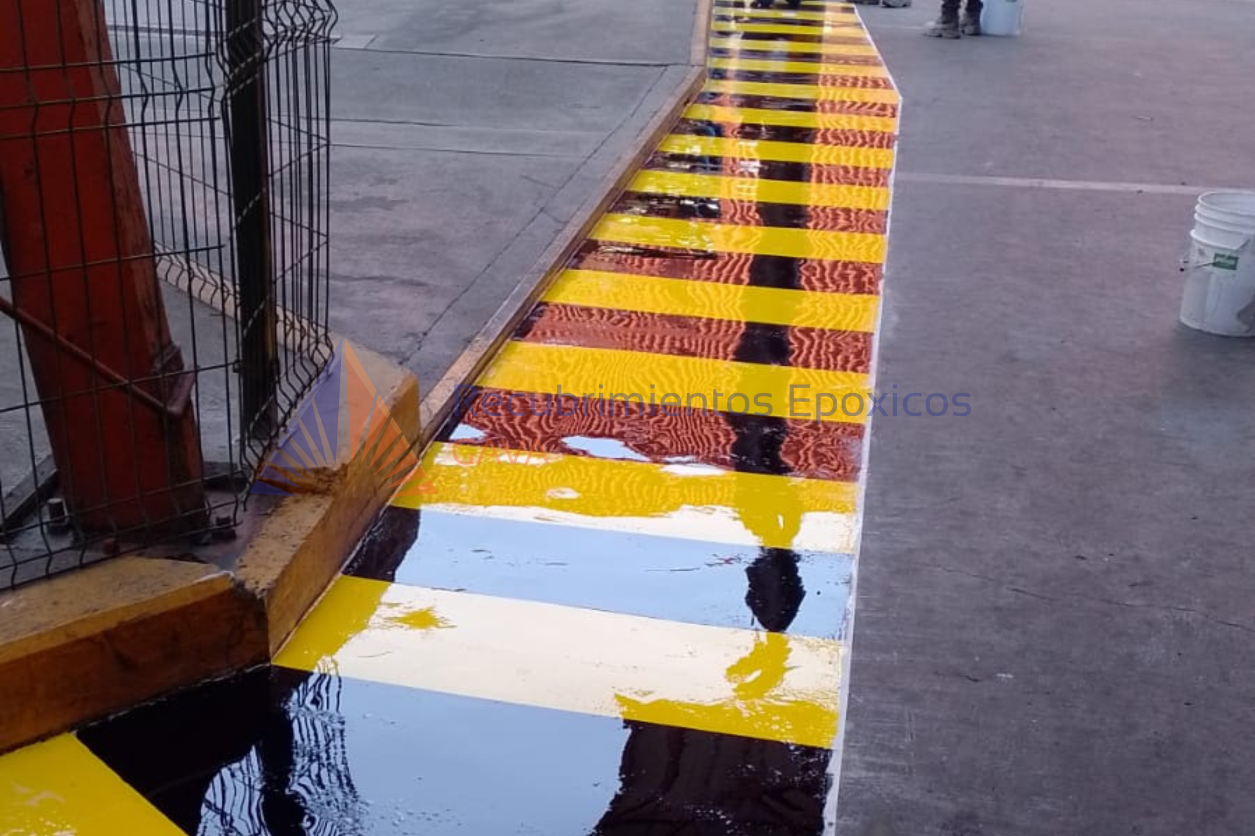 Señalización en el suelo de líneas amarillas y negras, probablemente para marcar zona de mantenimiento o peligro, en una acera o calle.