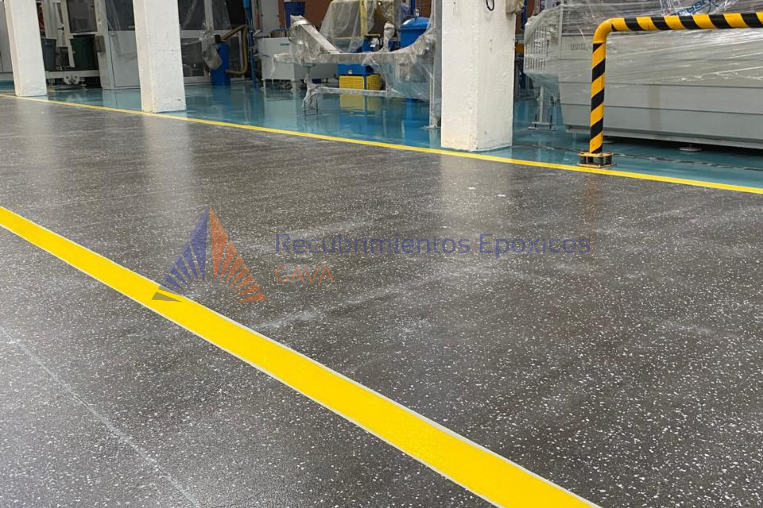 Piso de fábrica con línea amarilla y logotipo de Recubrimientos Epóxicos GAVA en la esquina inferior izquierda.